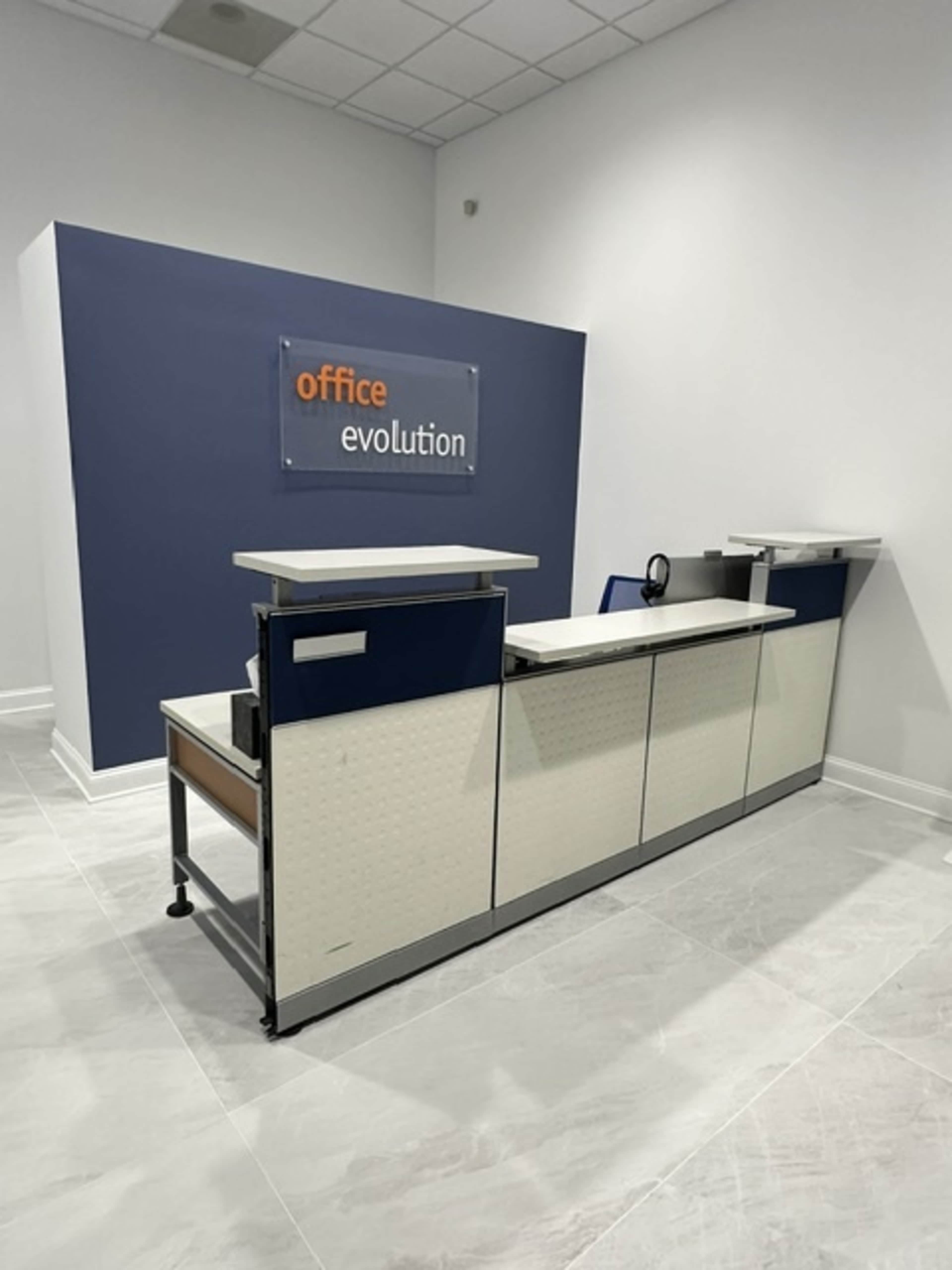 A reception desk in an office space with a wall sign that reads "office evolution."