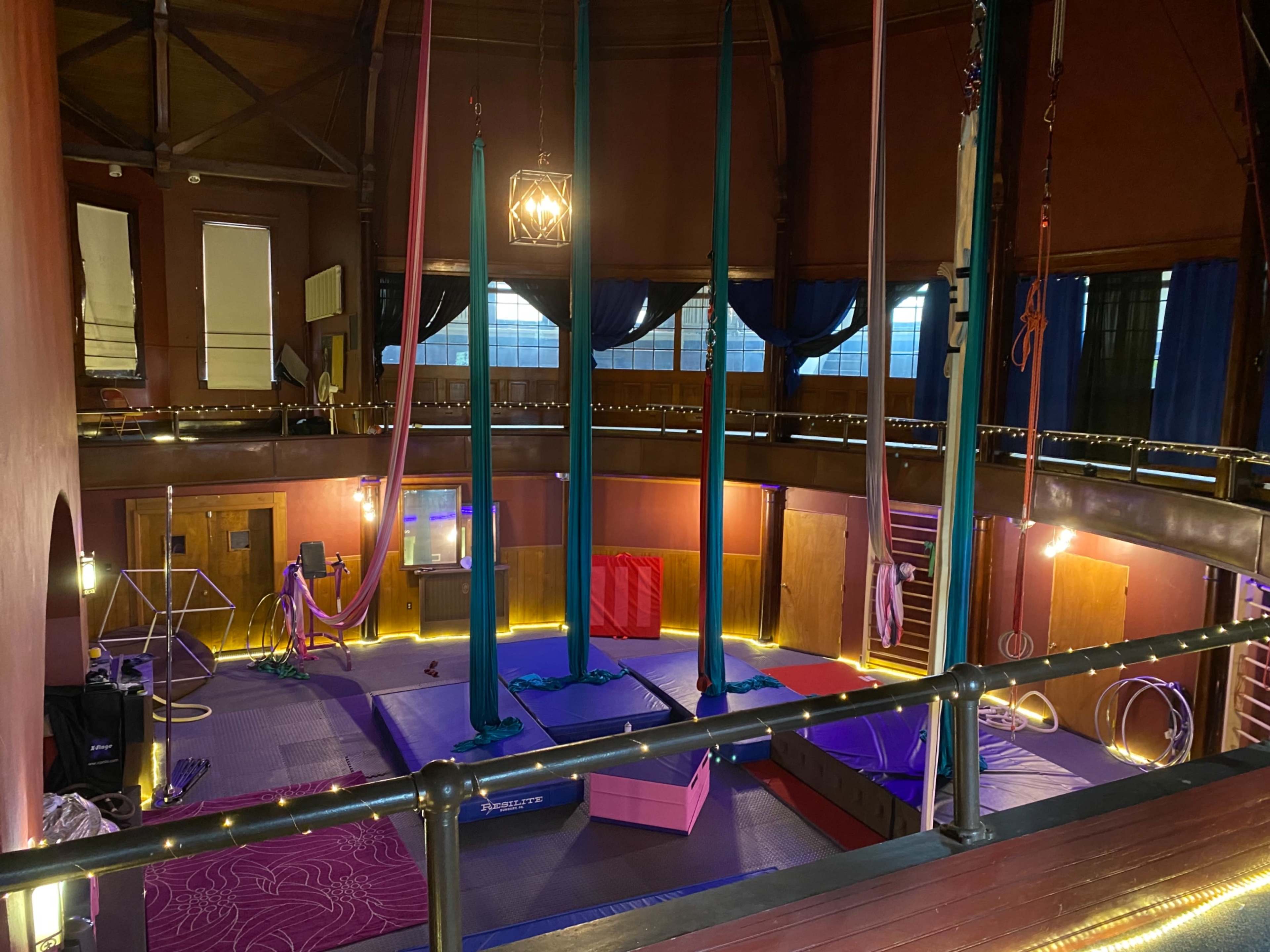 An indoor aerial performance space with multiple silks hanging from the ceiling, illuminated by soft lights.