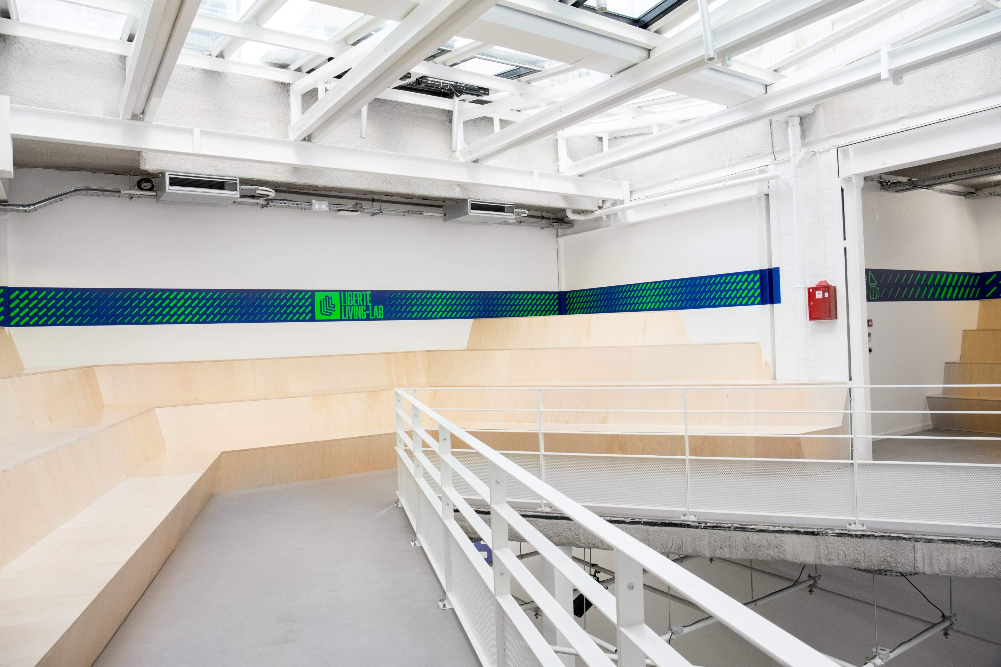 A modern interior space with wooden tiered seating and a balcony railing, featuring a colorful wall design that reads "Creativity Lab."