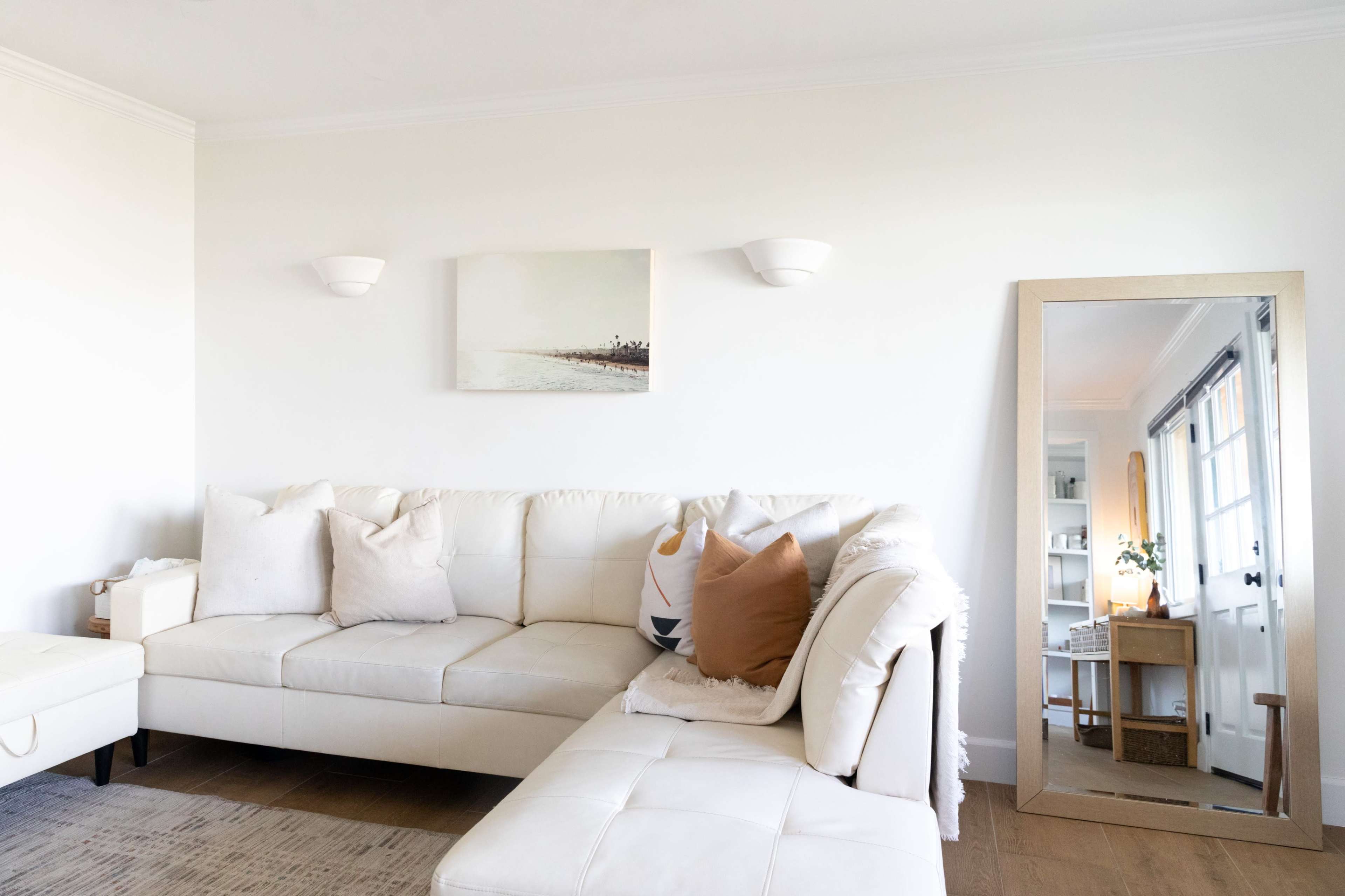 A modern living room features a white sectional couch with decorative pillows and a large mirror against the wall.