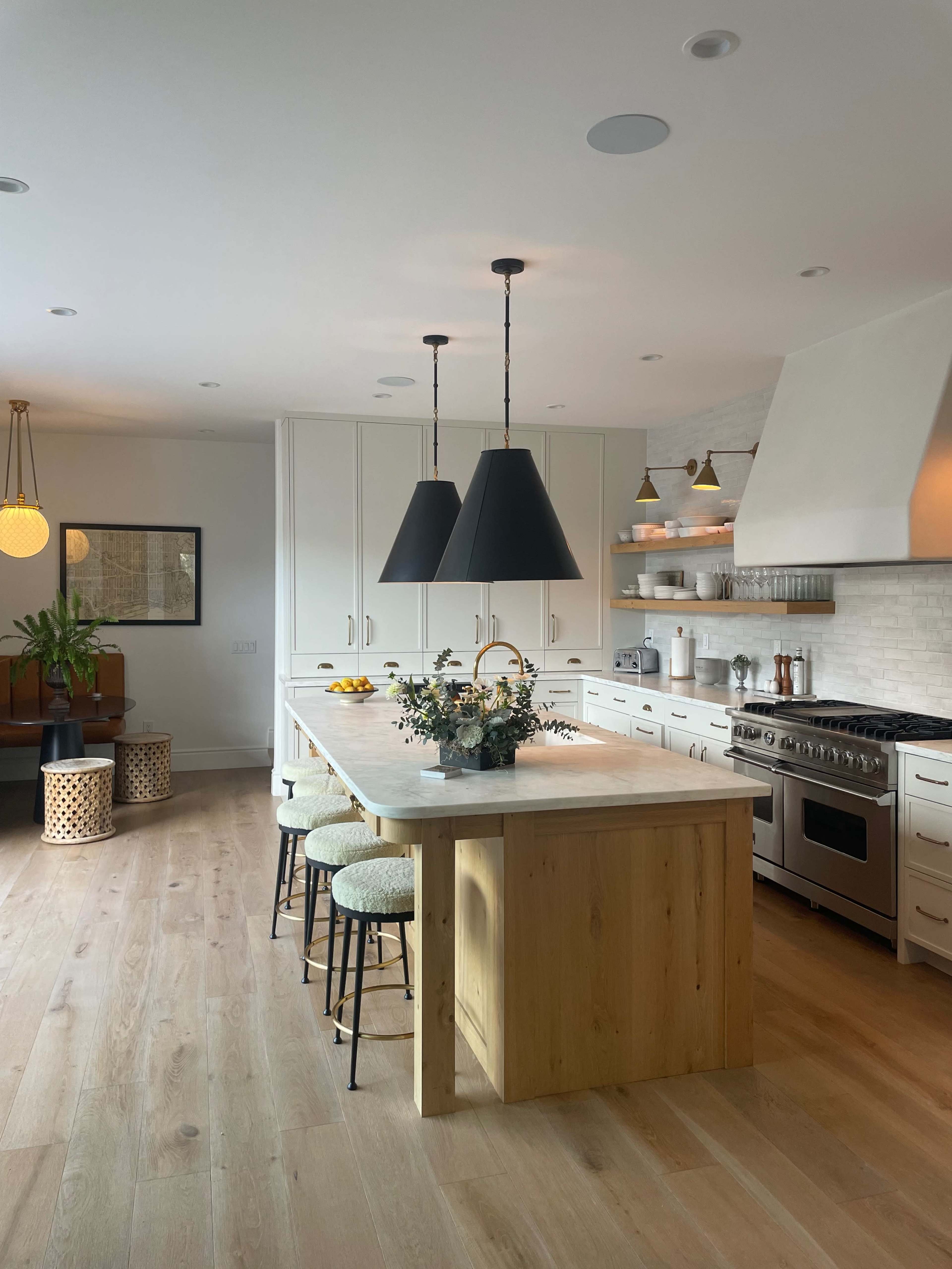 A modern kitchen features a large wooden island with three bar stools, black pendant lights, and stainless steel appliances.