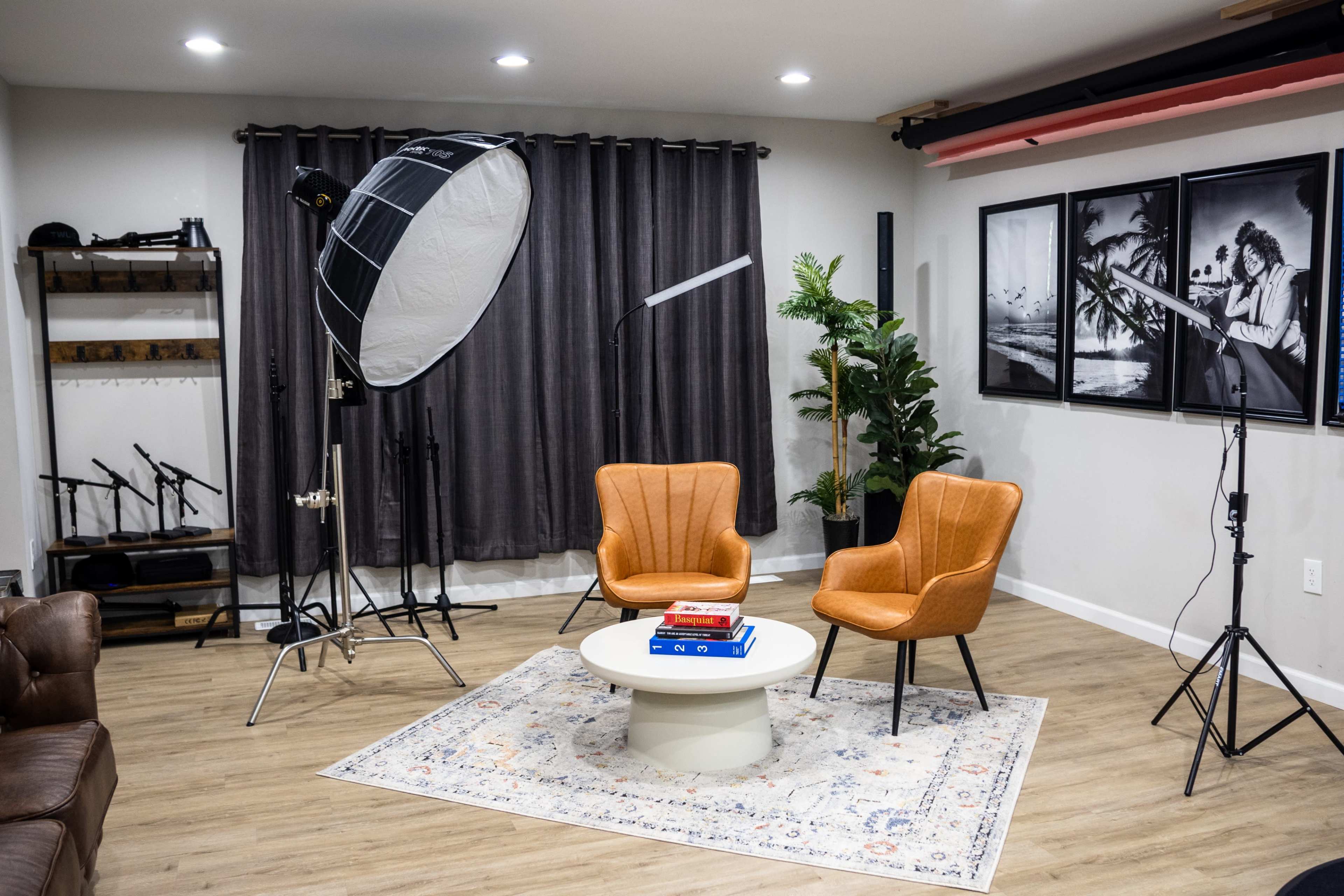 A well-lit indoor setting with two orange armchairs positioned around a circular coffee table, accompanied by photography equipment and decorative plants in a stylish studio space.