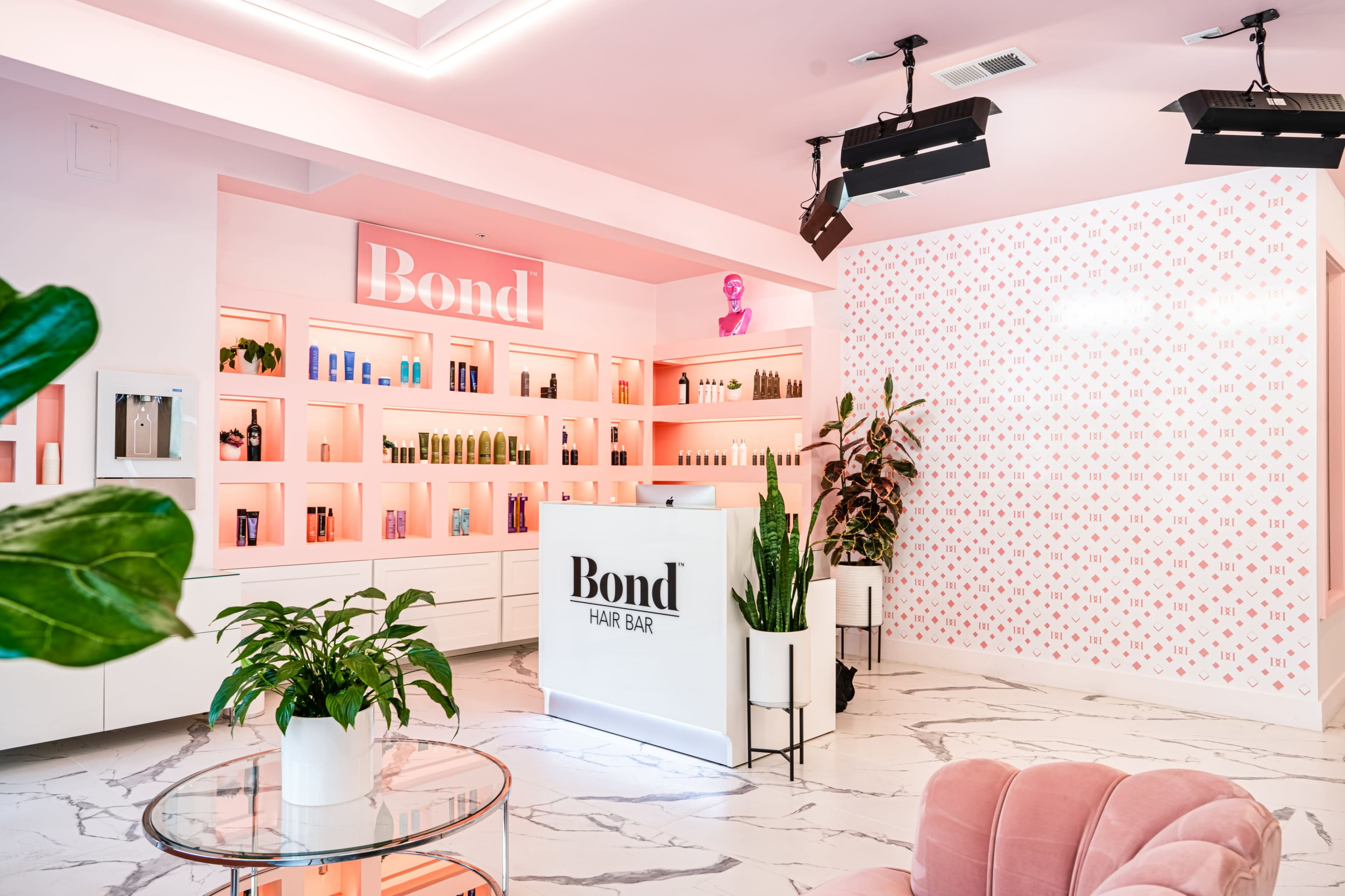 A modern hair salon reception area with a white and pink color scheme, featuring a front desk, shelves of hair products, and pink decor.