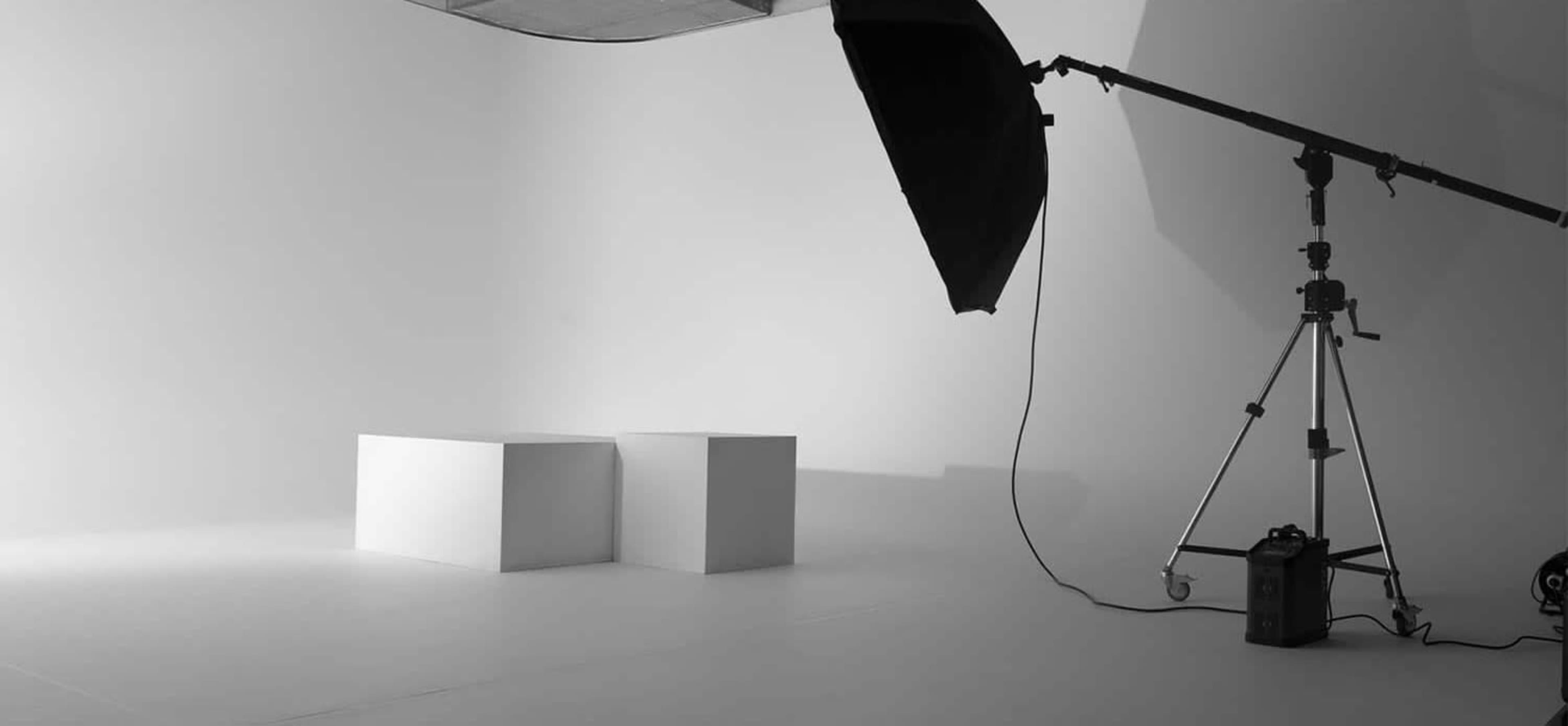 A minimalistic photography studio with two white cubes, a large softbox, and a light stand on a white backdrop.