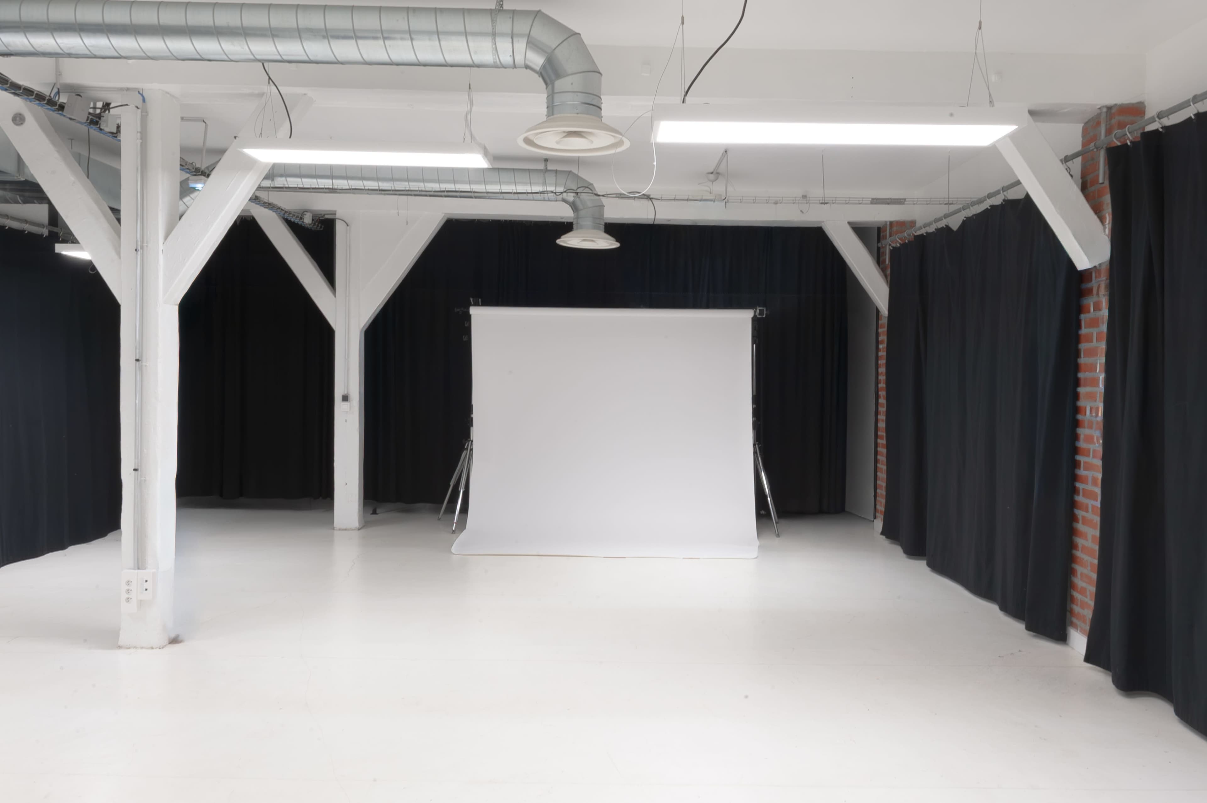 The image shows a spacious, well-lit studio with a white backdrop at the center and black curtains lining the walls.