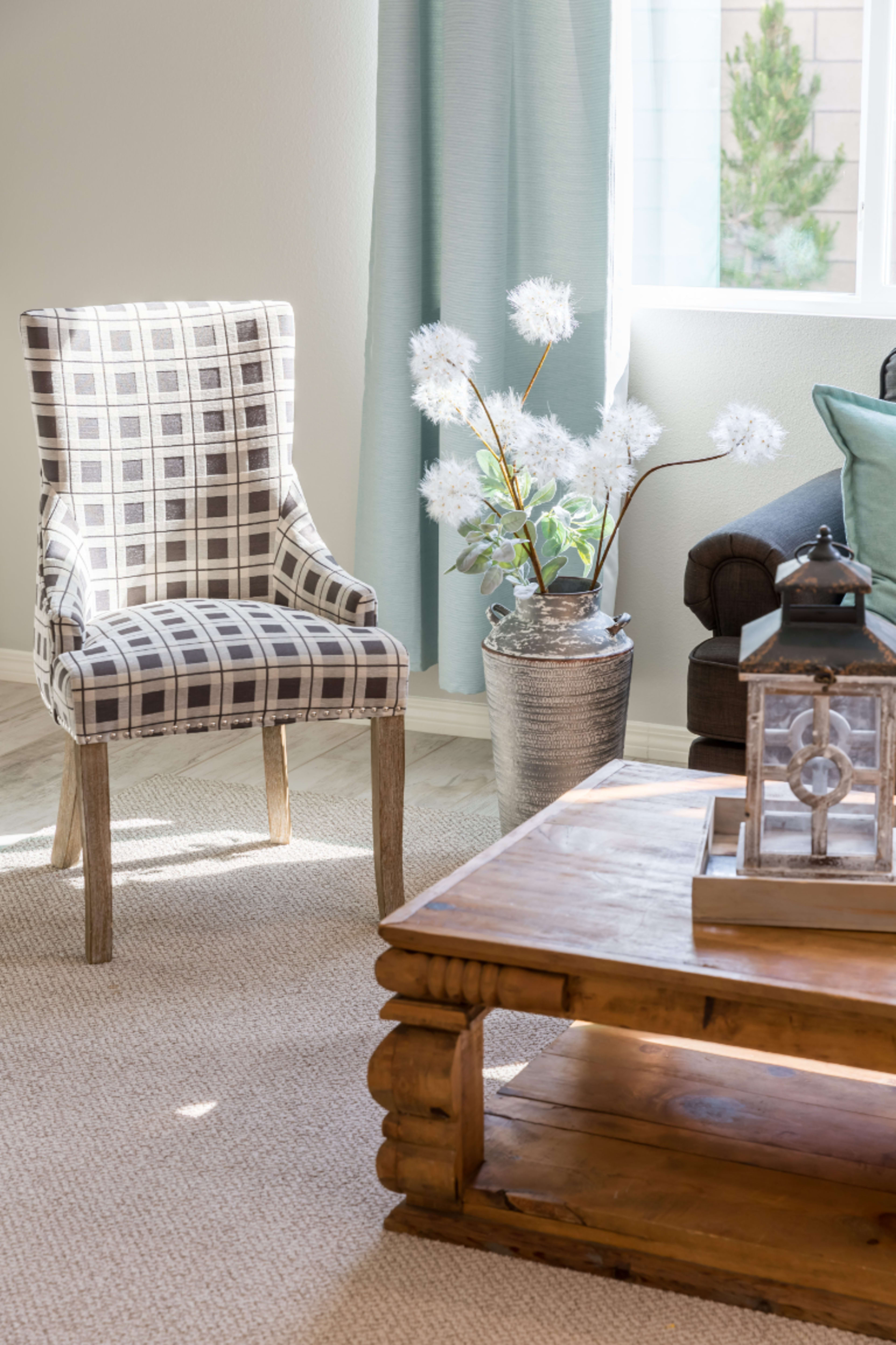 A checkered chair sits next to a wooden coffee table, while a decorative plant in a metallic pot and a lantern complete the living room scene.