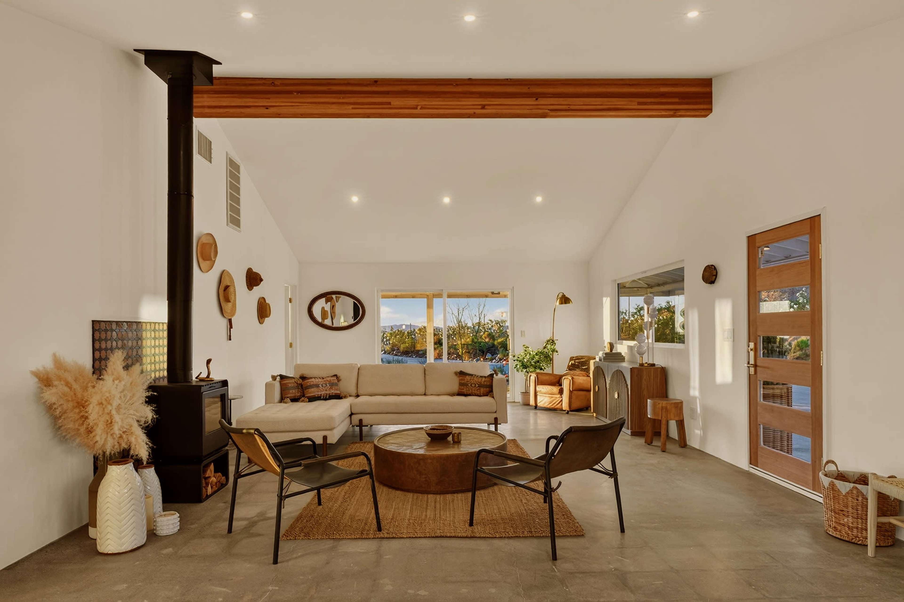 The image features a modern living room with a light-colored sofa, two black chairs, a round coffee table, and windows that provide a view of the outdoors.