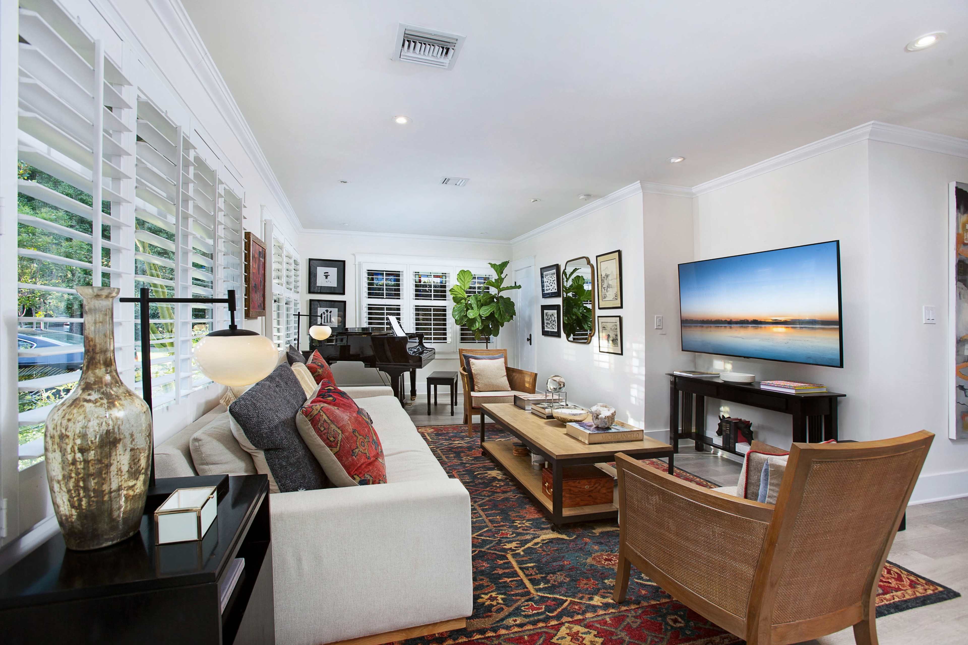 A cozy living room with a sofa, decorative pillows, a coffee table, and a television mounted on the wall, surrounded by framed artwork and plants.