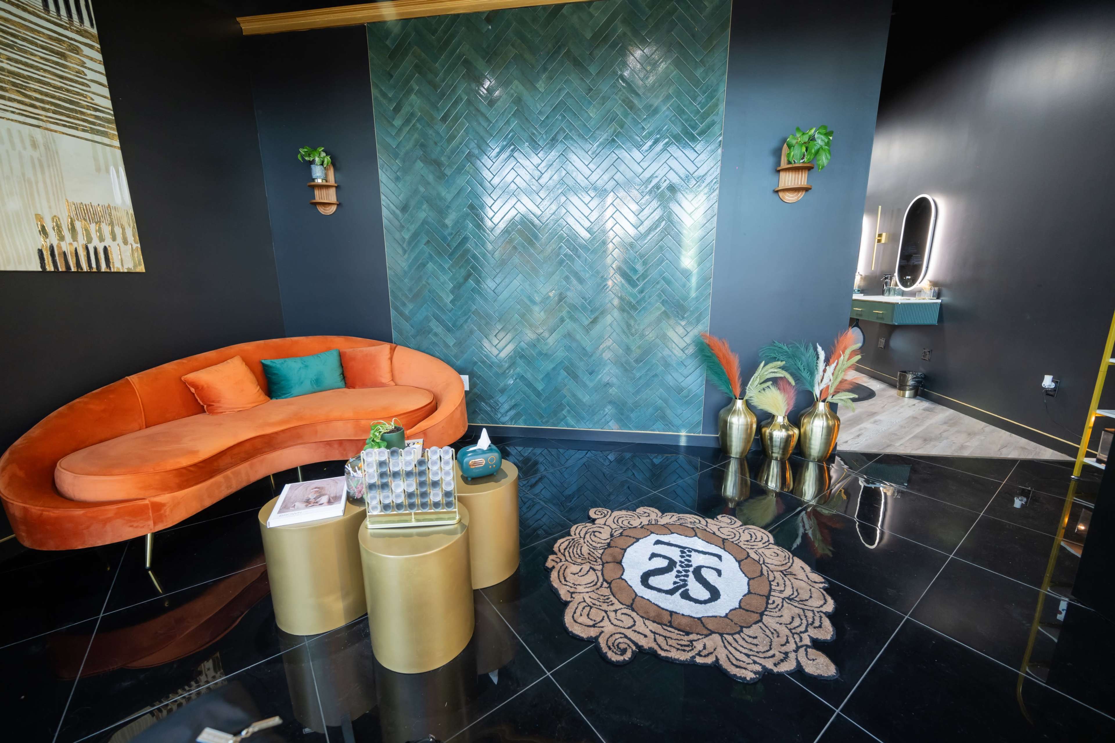 The image depicts a modern interior space with a curved orange sofa, a dark tile floor, and a textured green wall, accompanied by decorative plants and a vanity area in the background.