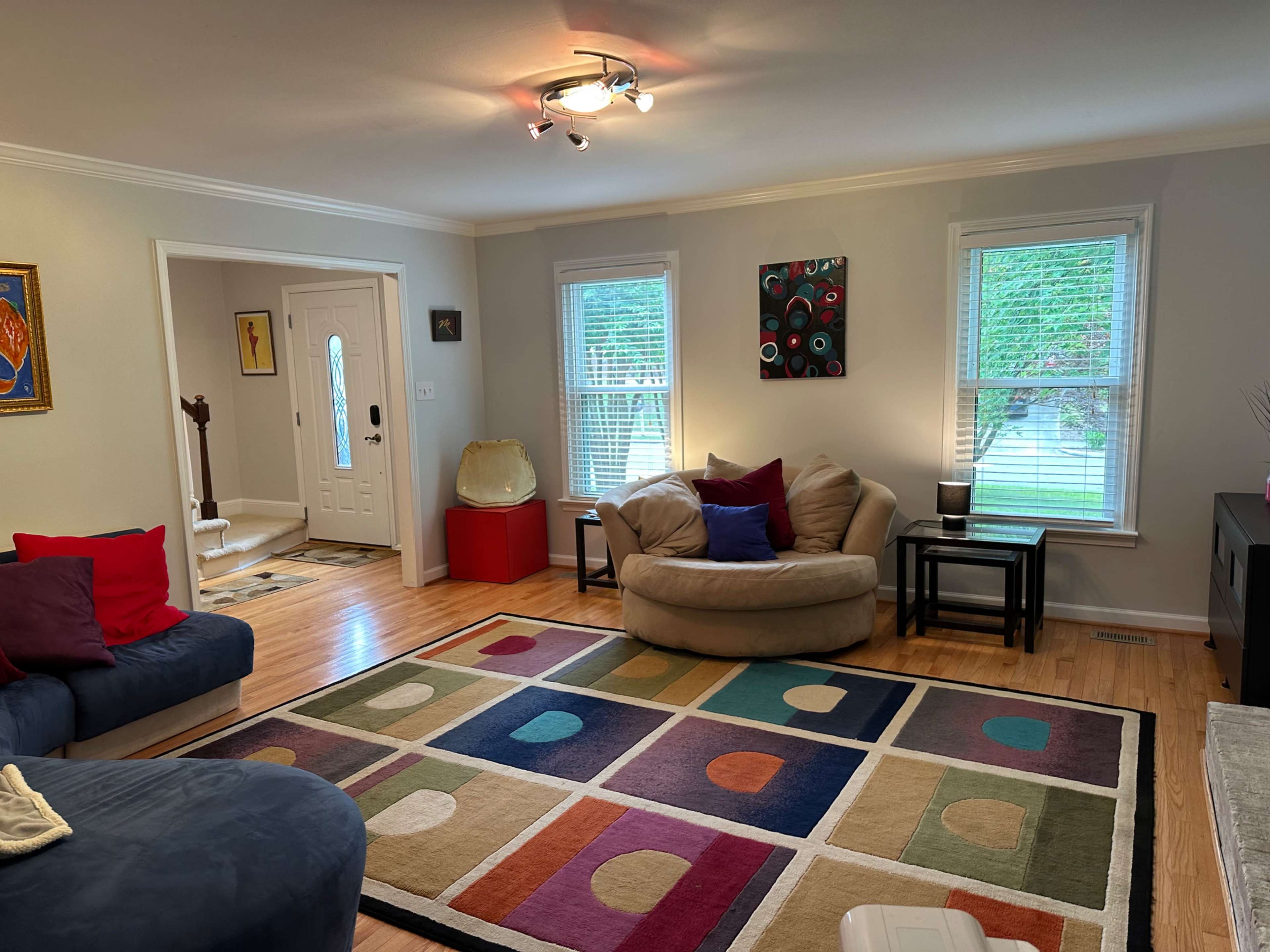 The living room features a beige bean bag chair, a colorful area rug, and a blue couch, with large windows allowing natural light in.
