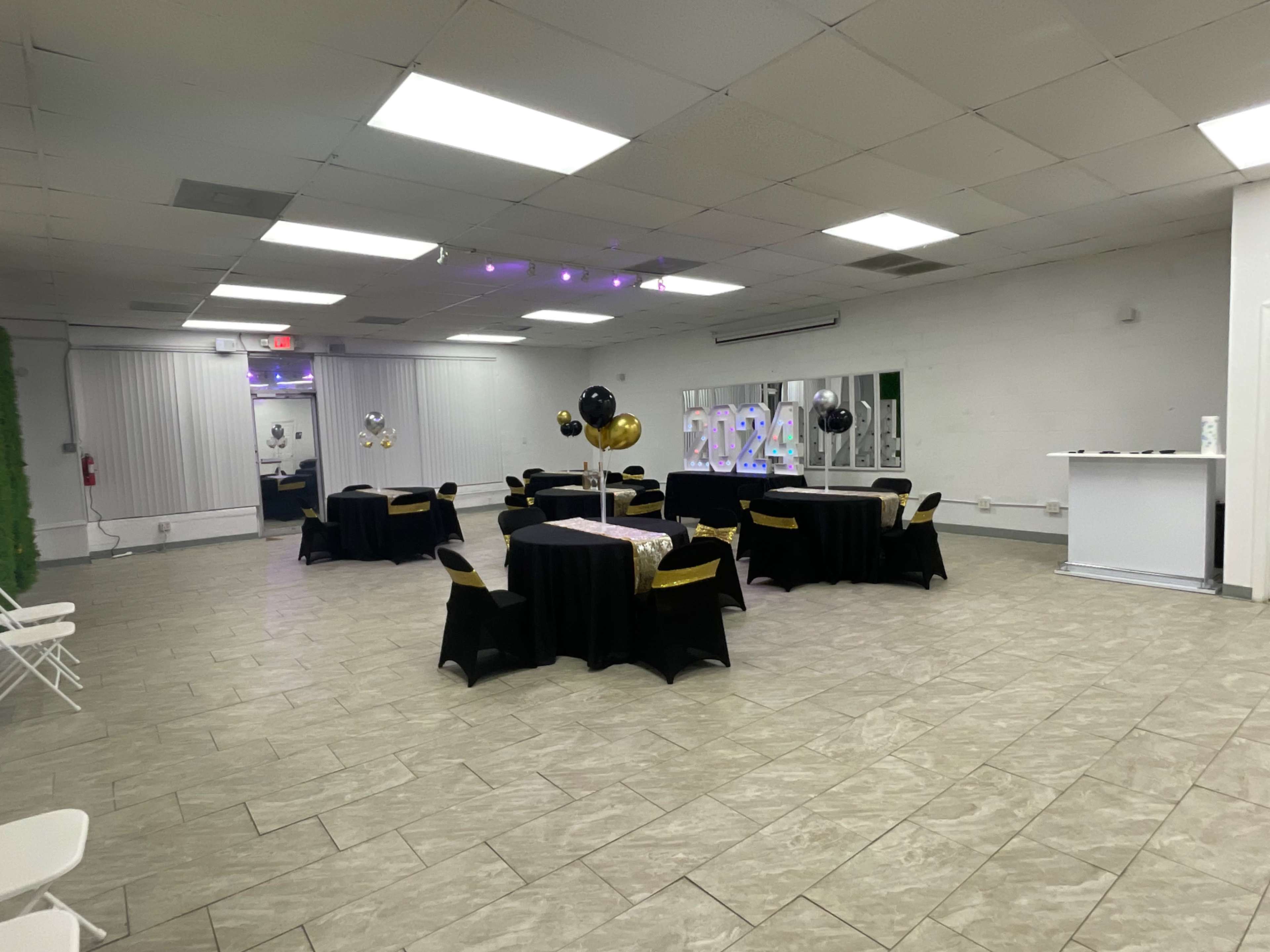 A spacious event room decorated with black and gold balloons, tables covered in black cloth, and a large "2024" display.