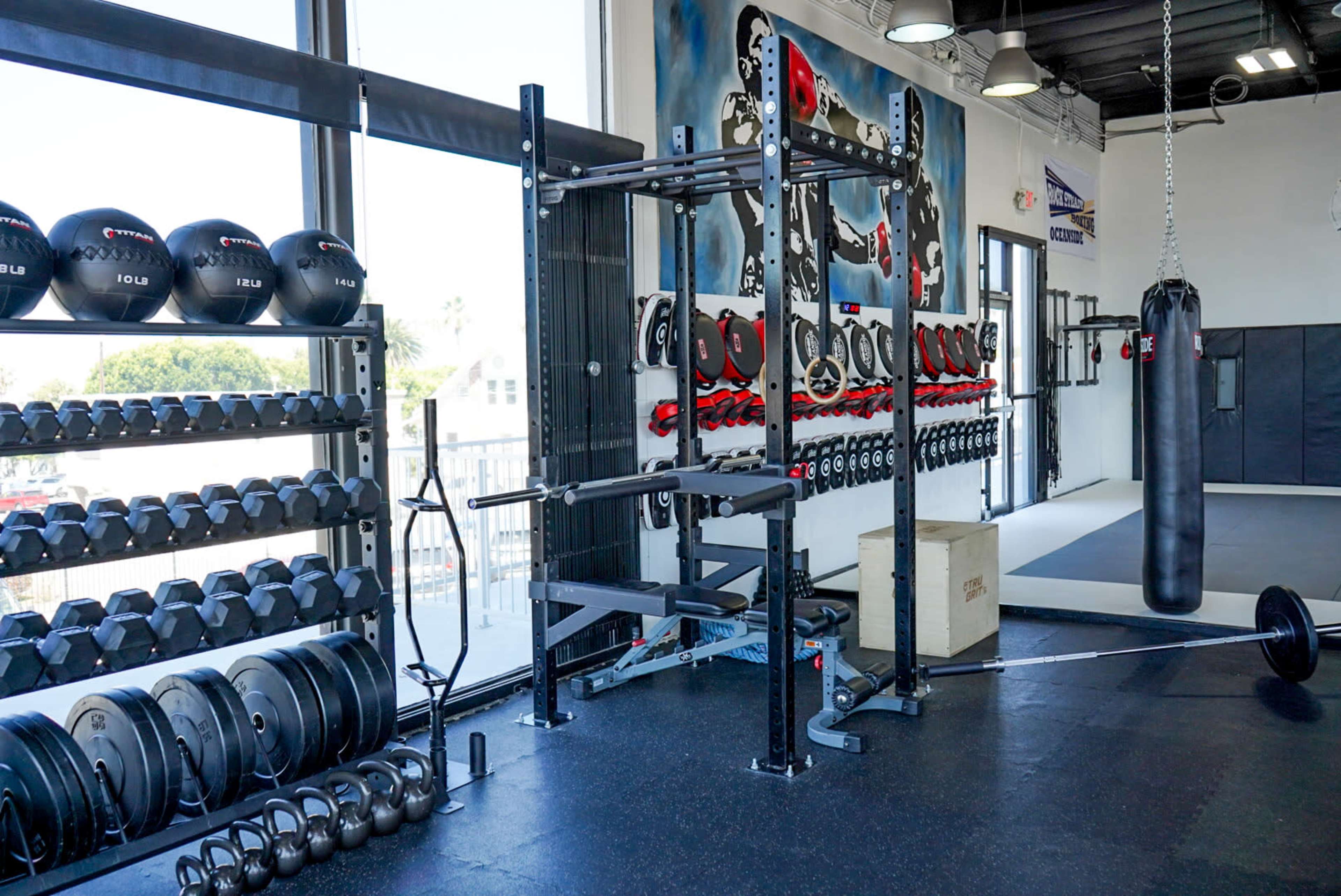 The gym features a variety of weightlifting equipment, including dumbbells, a power rack, a barbell, and a punching bag.