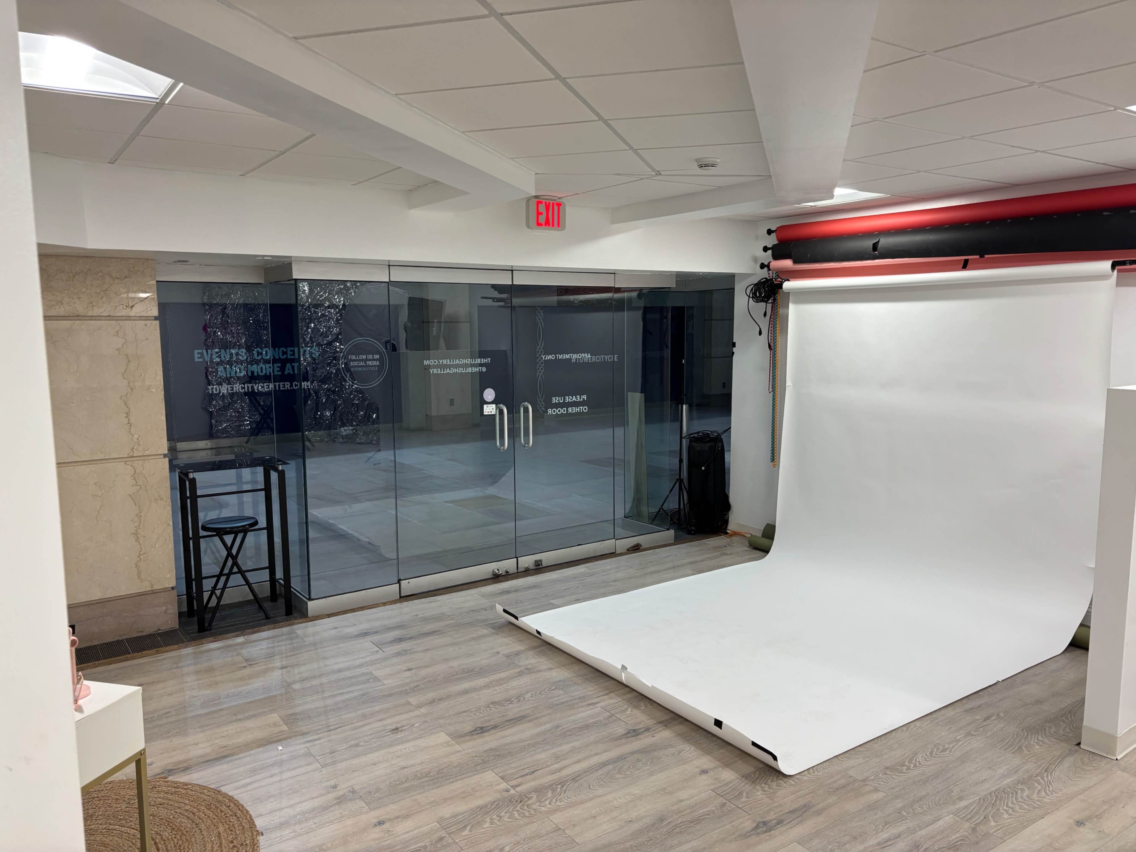 The image shows a studio space with a white photography backdrop and large glass doors leading to an outdoor area.