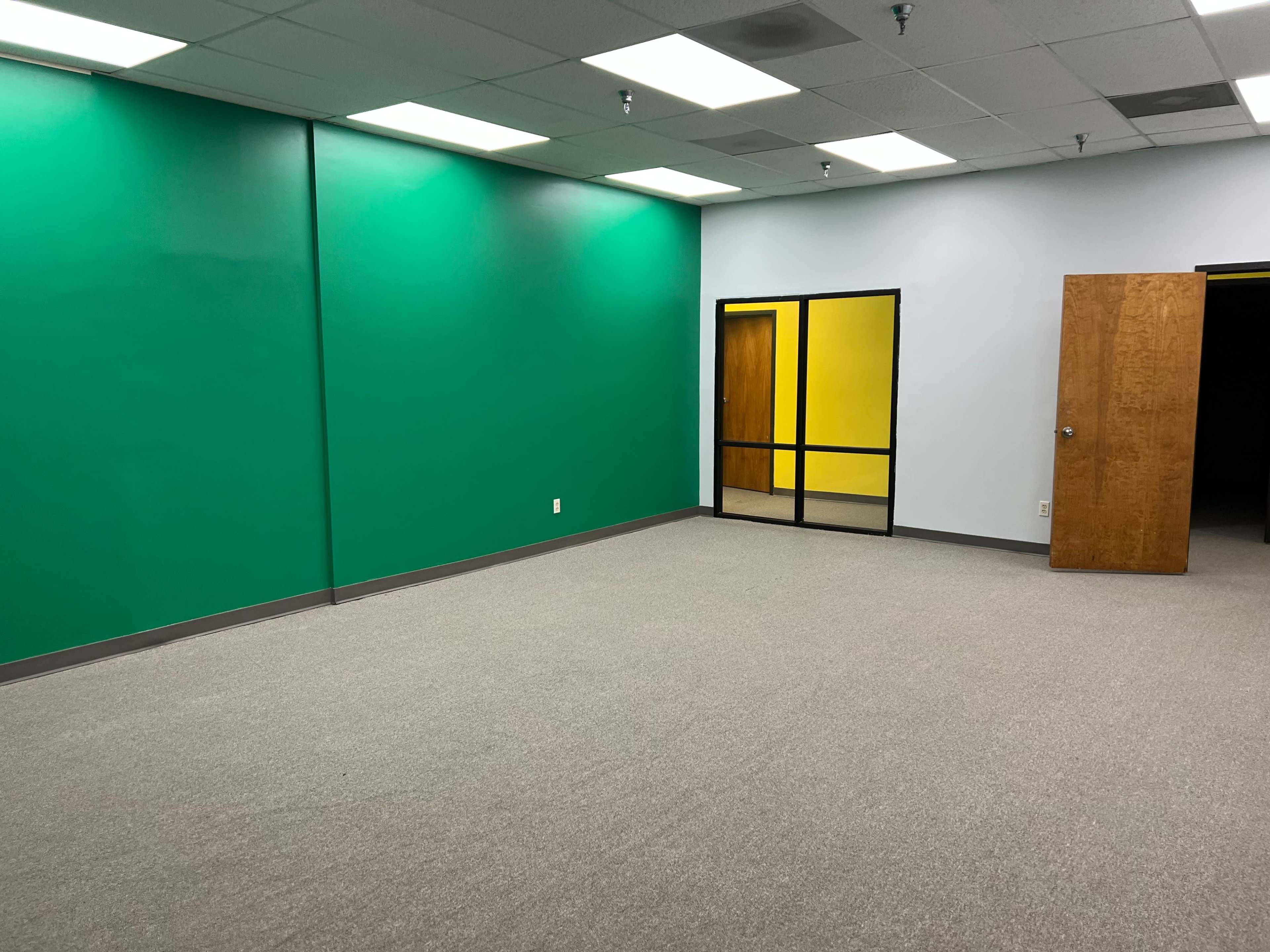 The image shows an empty room with green walls, gray carpeting, a yellow door frame, and a glass-panel door leading to another room.