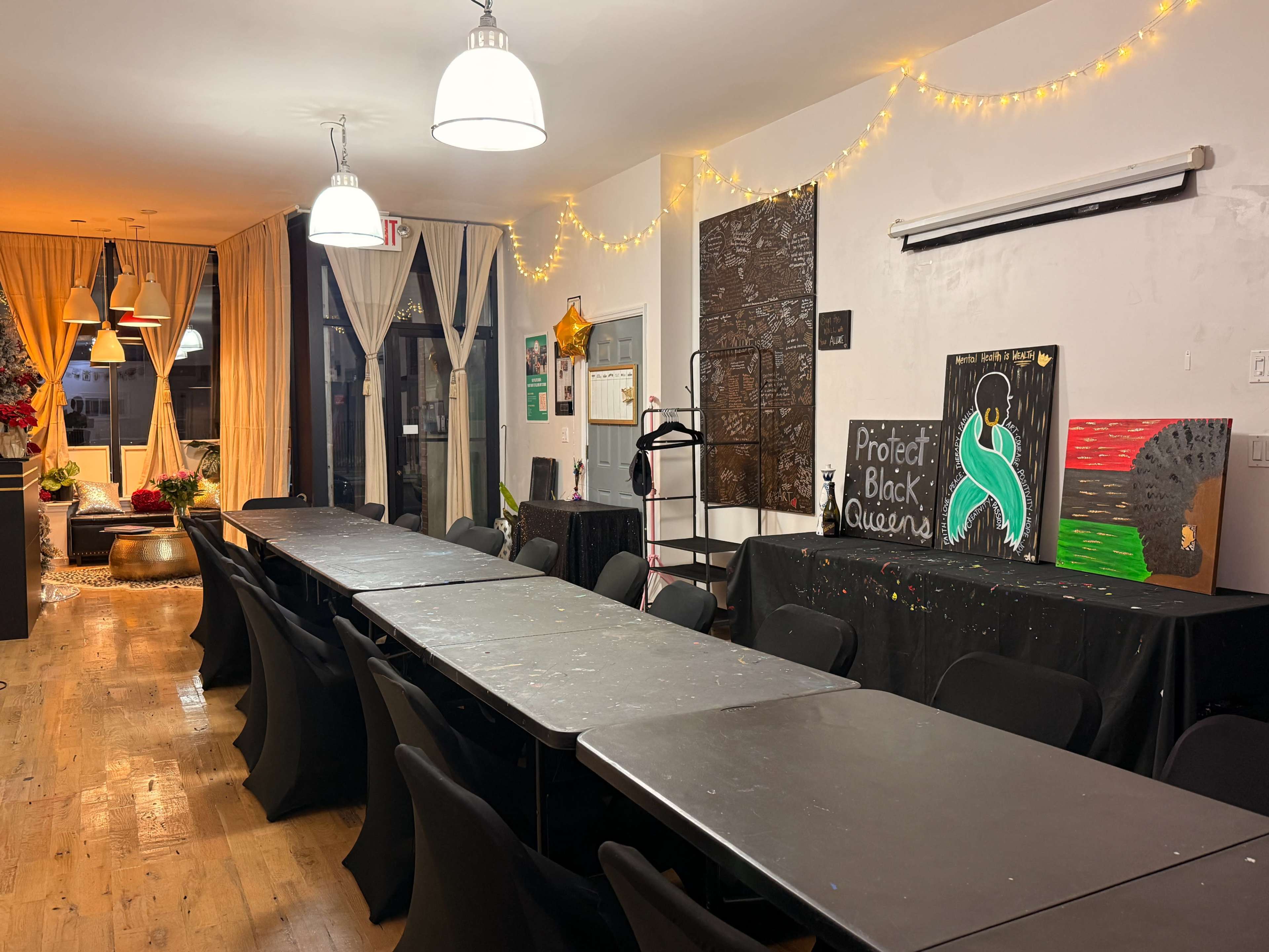 The image shows a brightly lit room with several long tables, black chairs, and decorations that include banners and artwork on the walls.