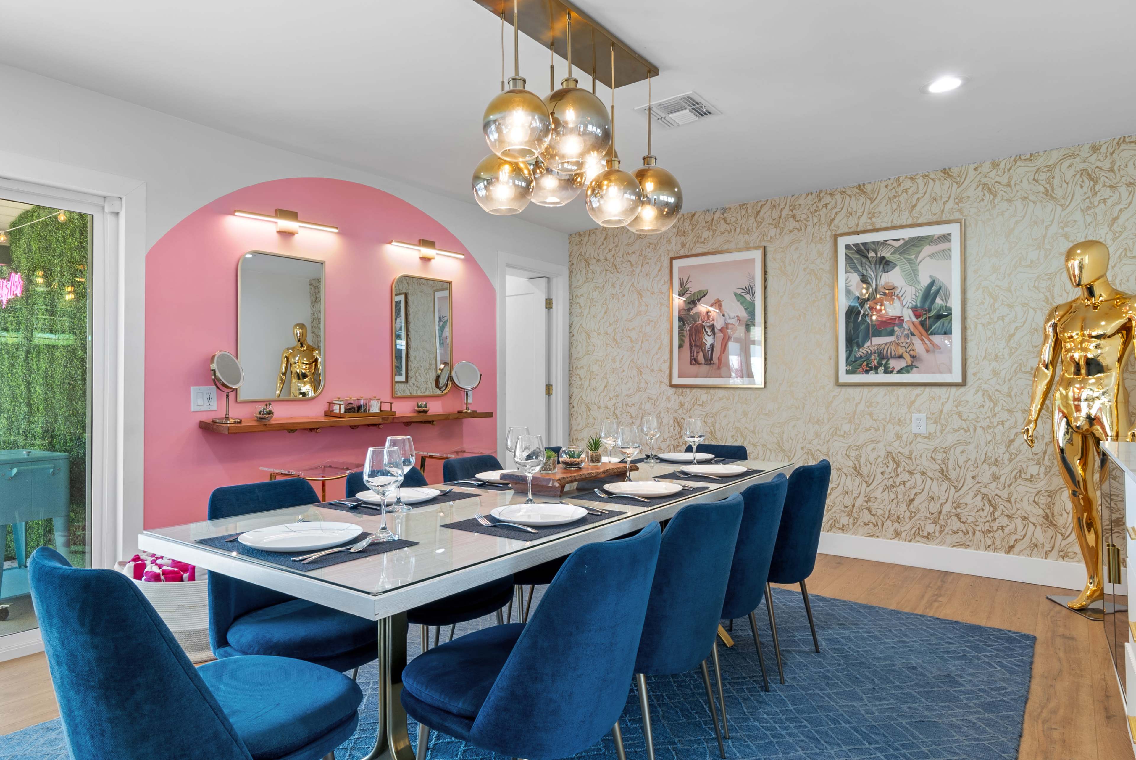 A modern dining room features a long table set with blue chairs, decorative wall art, and stylish lighting fixtures.