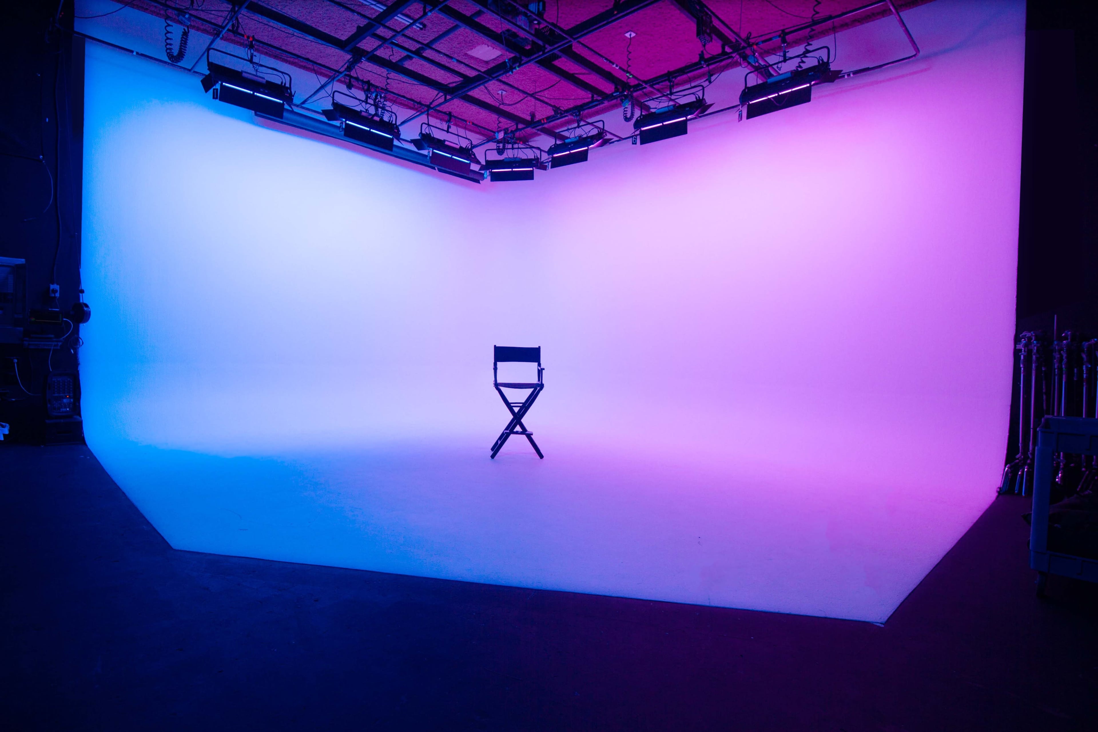 A director's chair is placed in the center of a brightly lit studio with a gradient background of blue and pink.