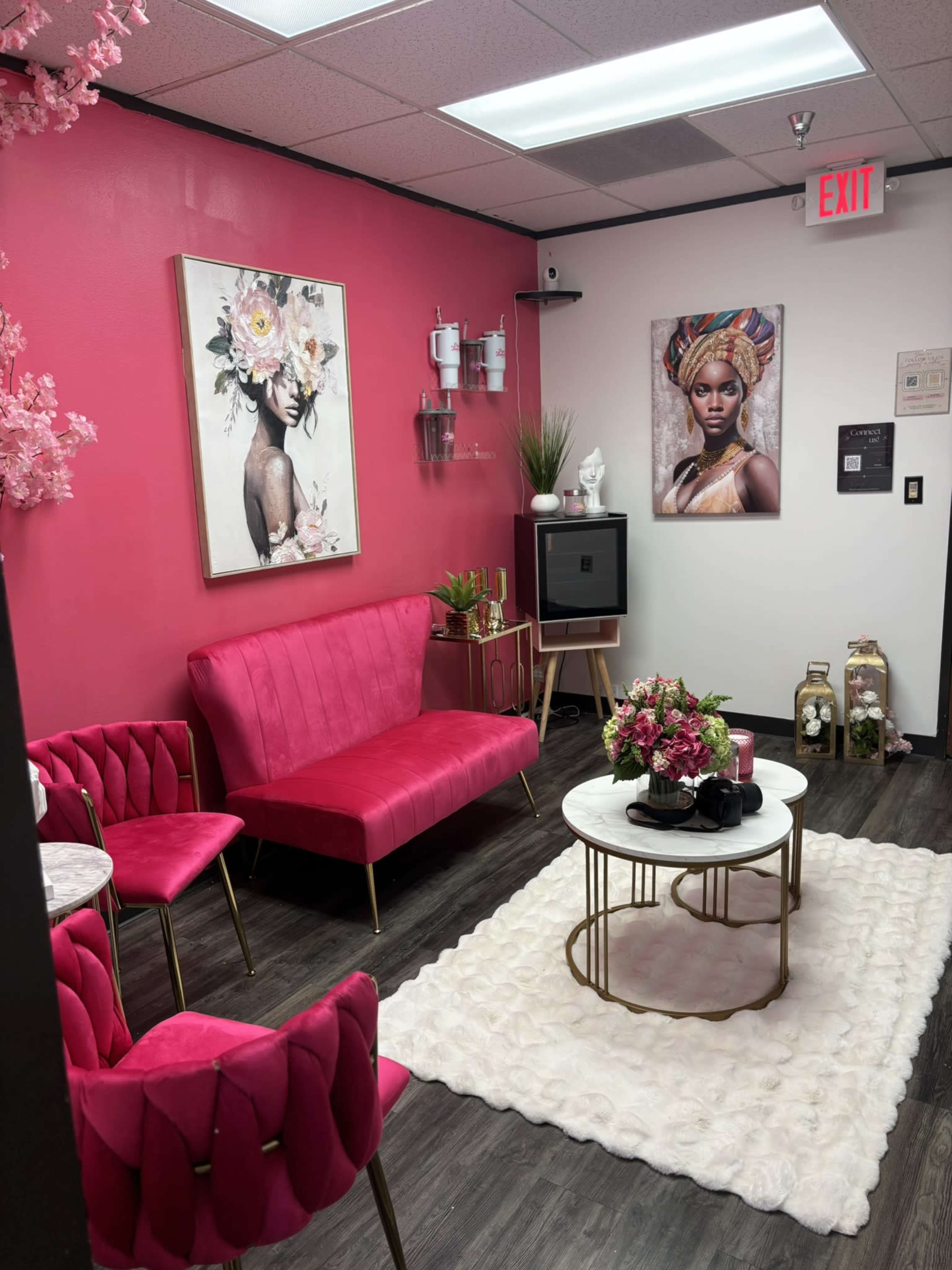 The image shows a stylized lounge area featuring a bright pink sofa, matching chairs, and a decorative coffee table, all set against pink and white walls adorned with framed artwork.