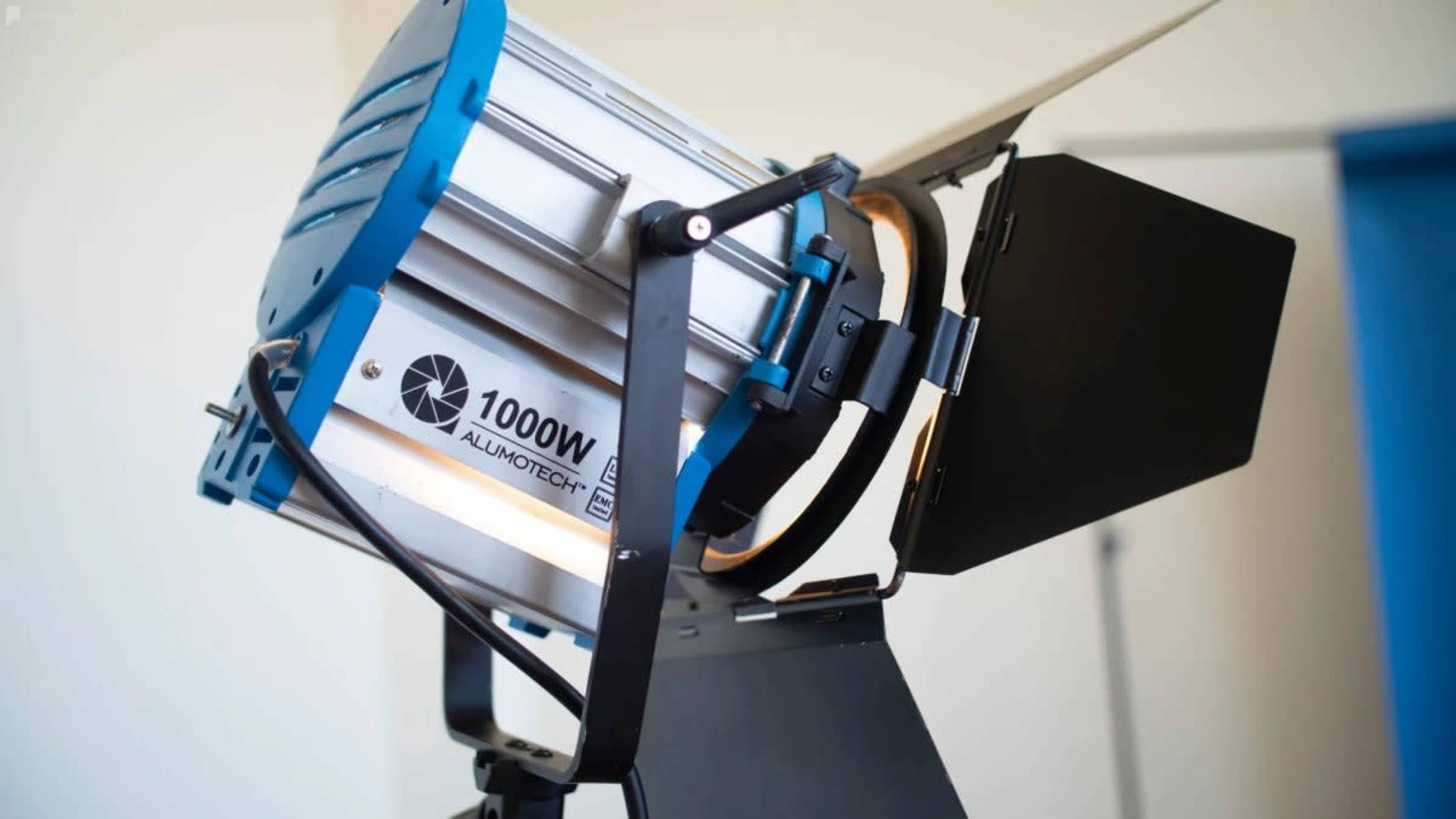 A professional 1000W film light mounted on a stand with a barn door attachment.
