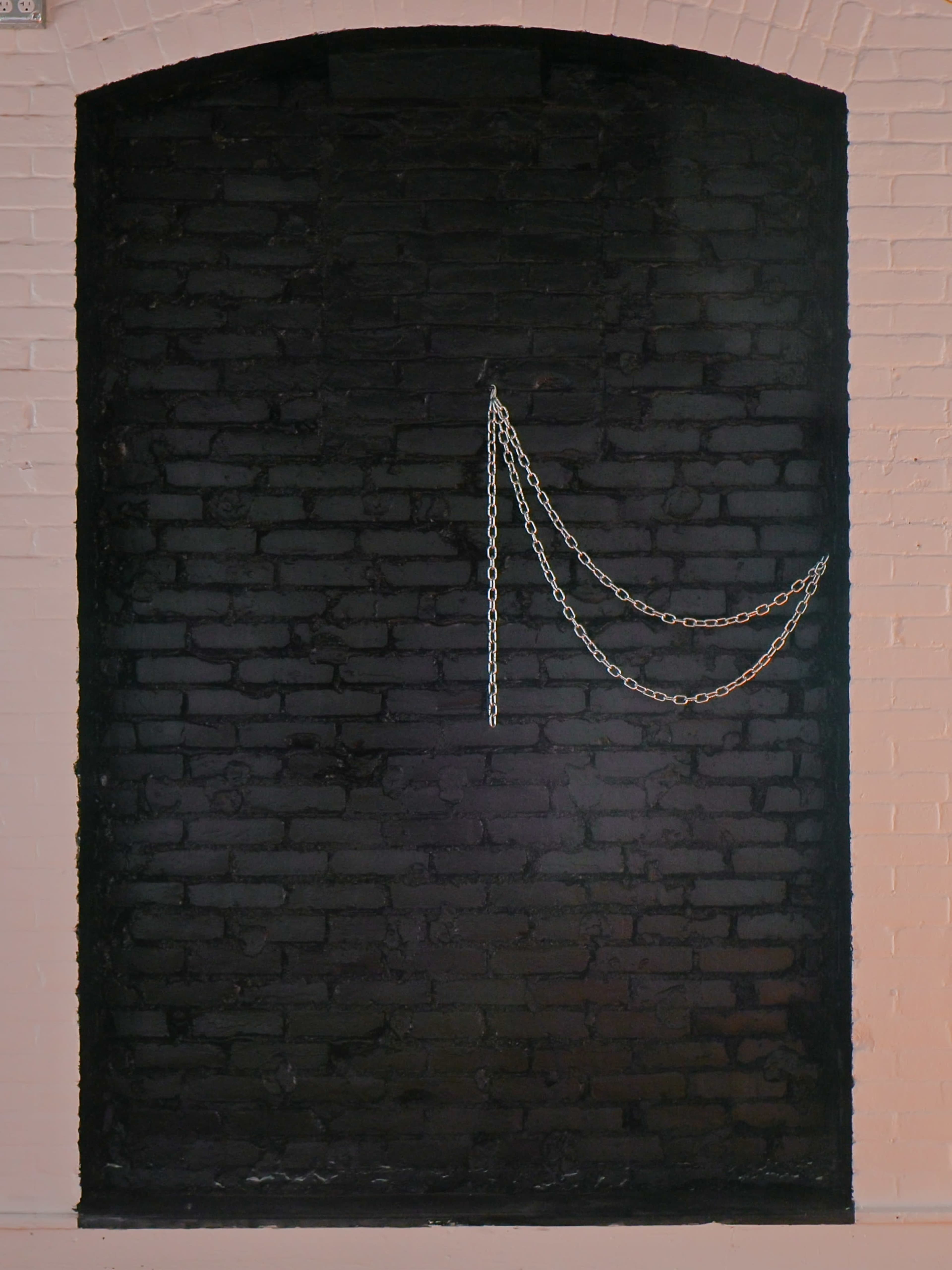 The image shows a black-painted brick wall with a silver chain draped across it.