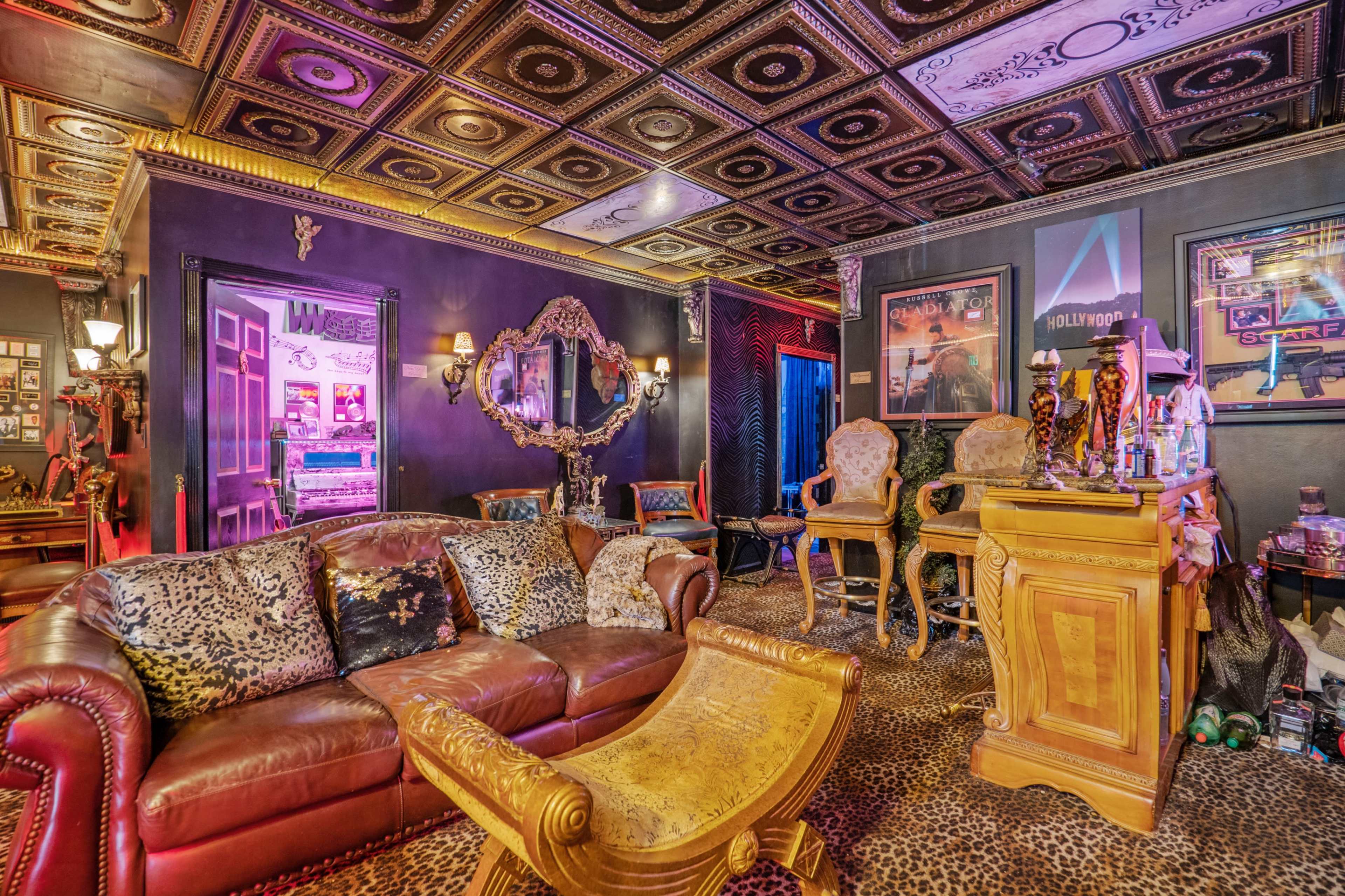 A luxurious room with a leather sofa, ornate chairs, a decorative mirror, and a ceiling featuring elaborate designs.