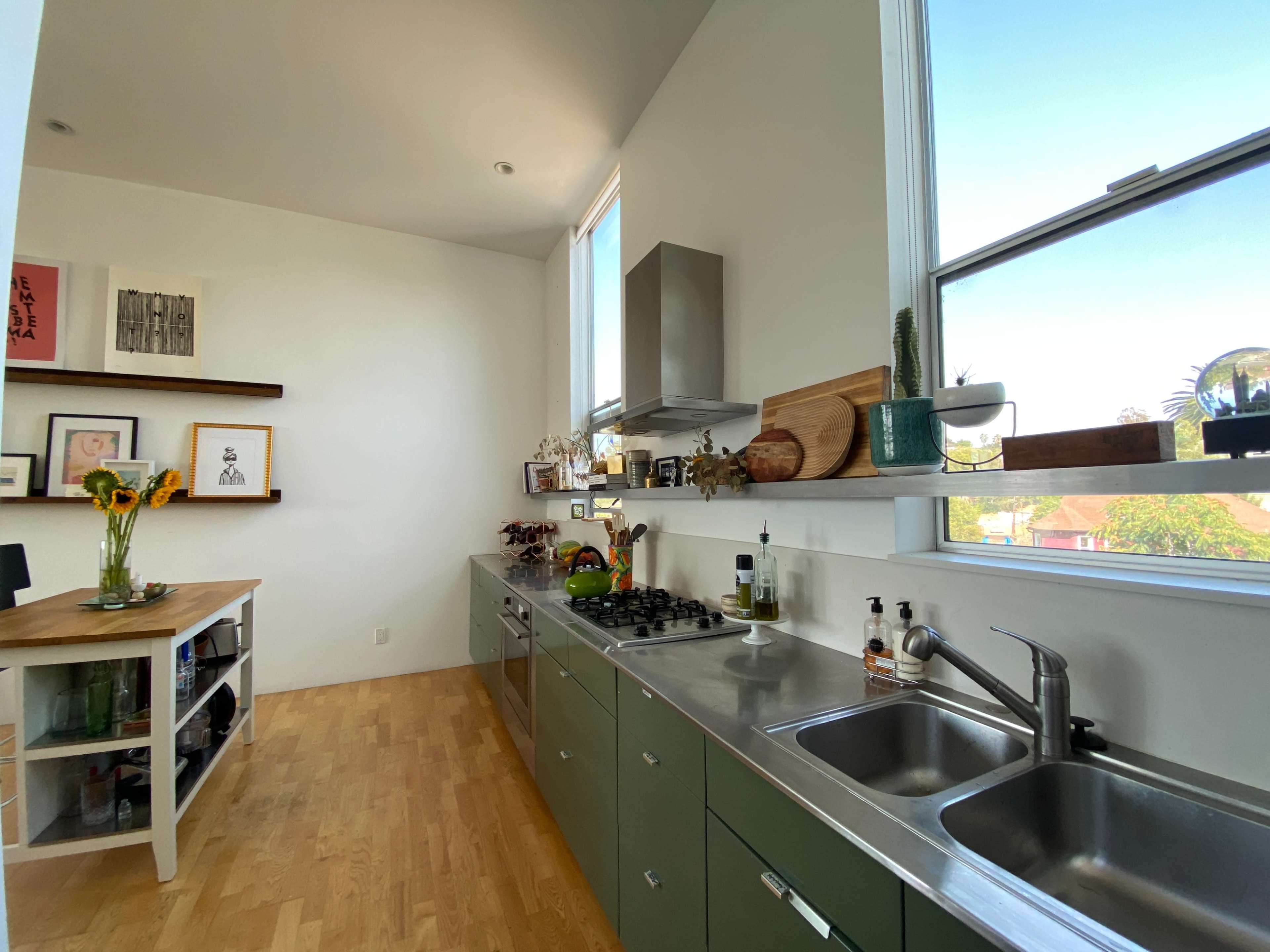 A modern kitchen with green cabinets, a stainless steel stove, and a wooden dining table against one wall, featuring various kitchen items and decorations.