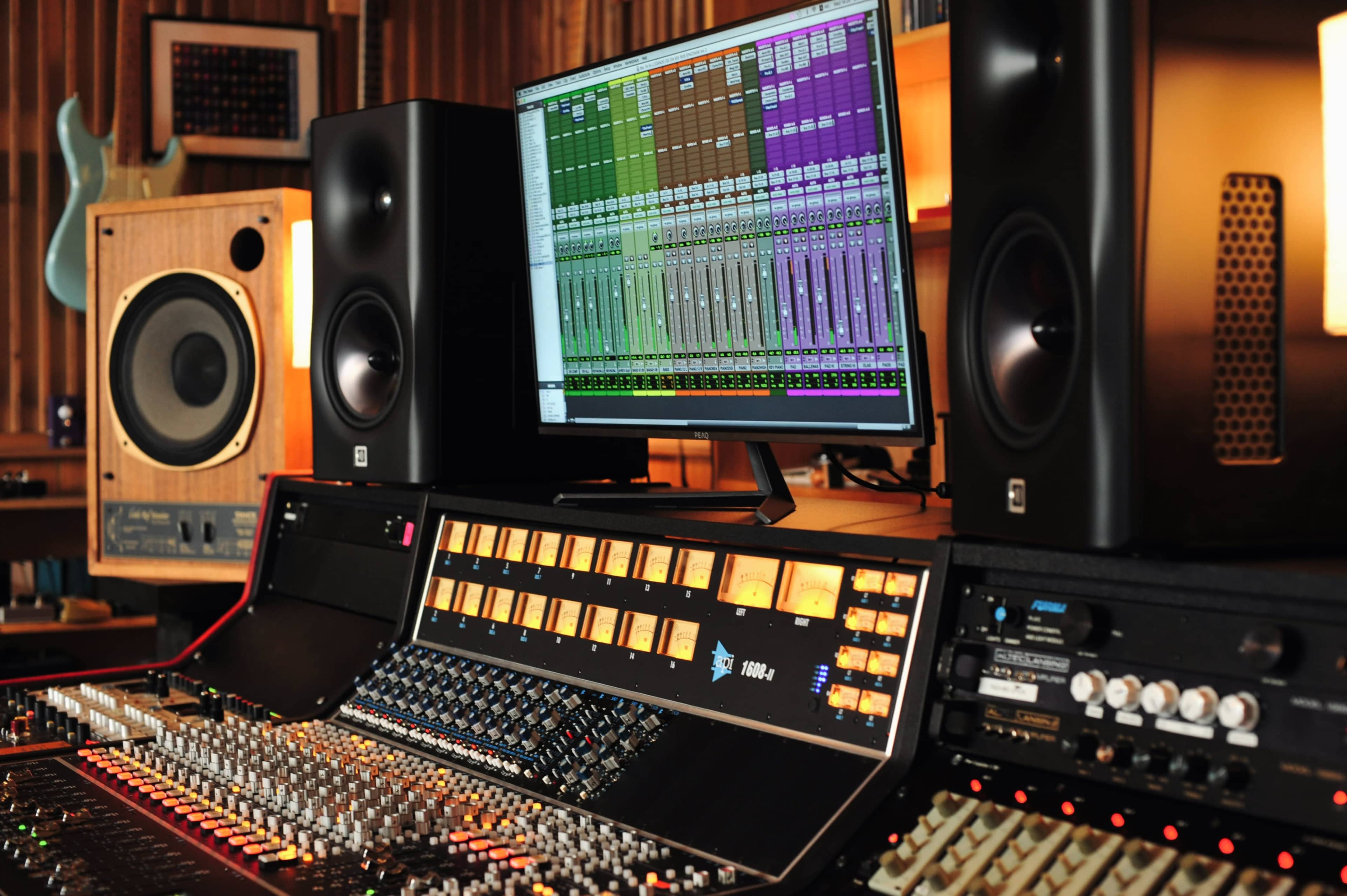 A professional audio mixing console with a computer monitor displaying digital audio tracks and studio monitors on either side in a recording studio.