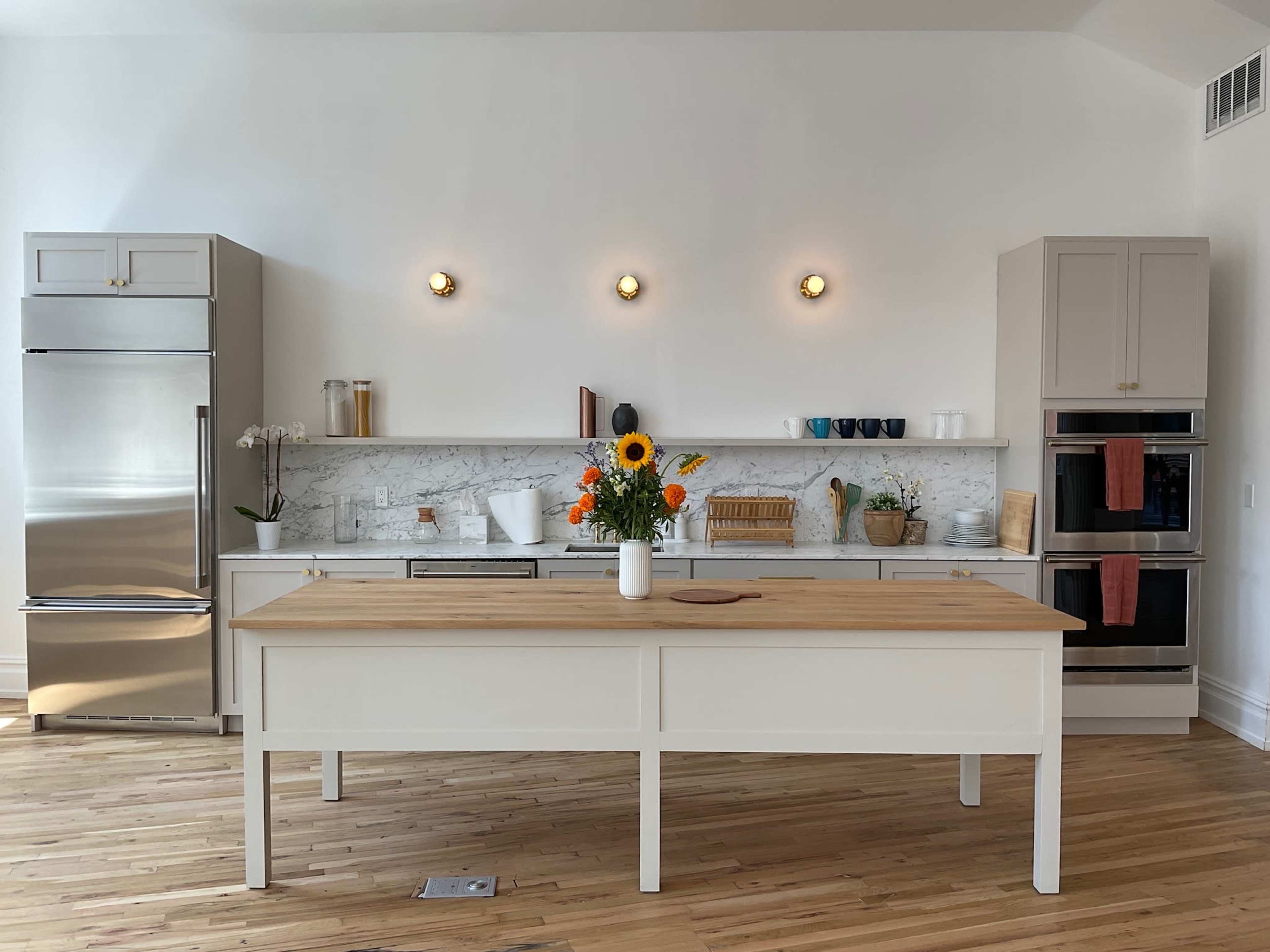 A modern kitchen features a central wooden island, stainless steel appliances, marble countertops, and a vase of sunflowers.