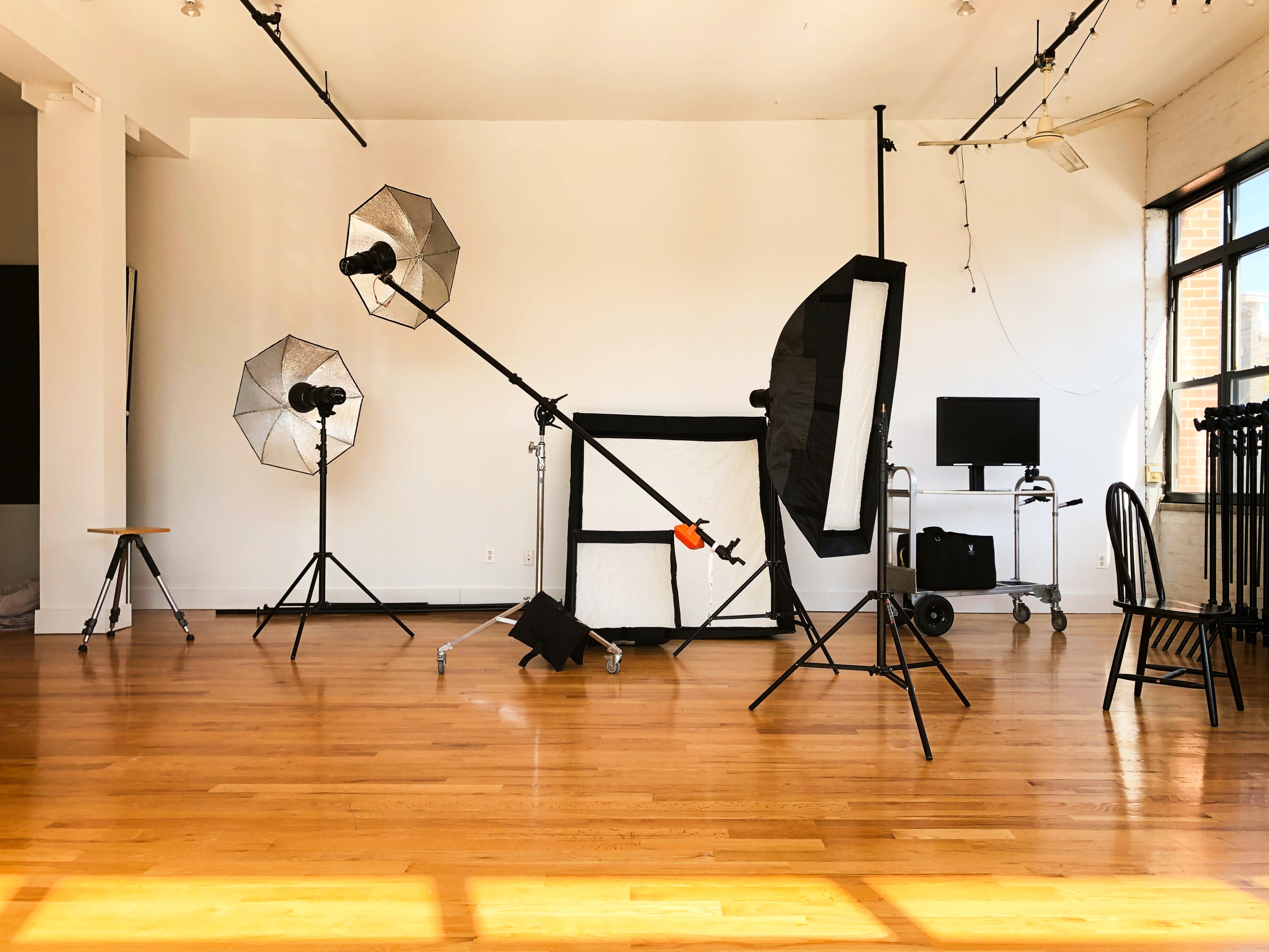 A photography studio features several lighting rigs, a backdrop, and various equipment arranged on a wooden floor.