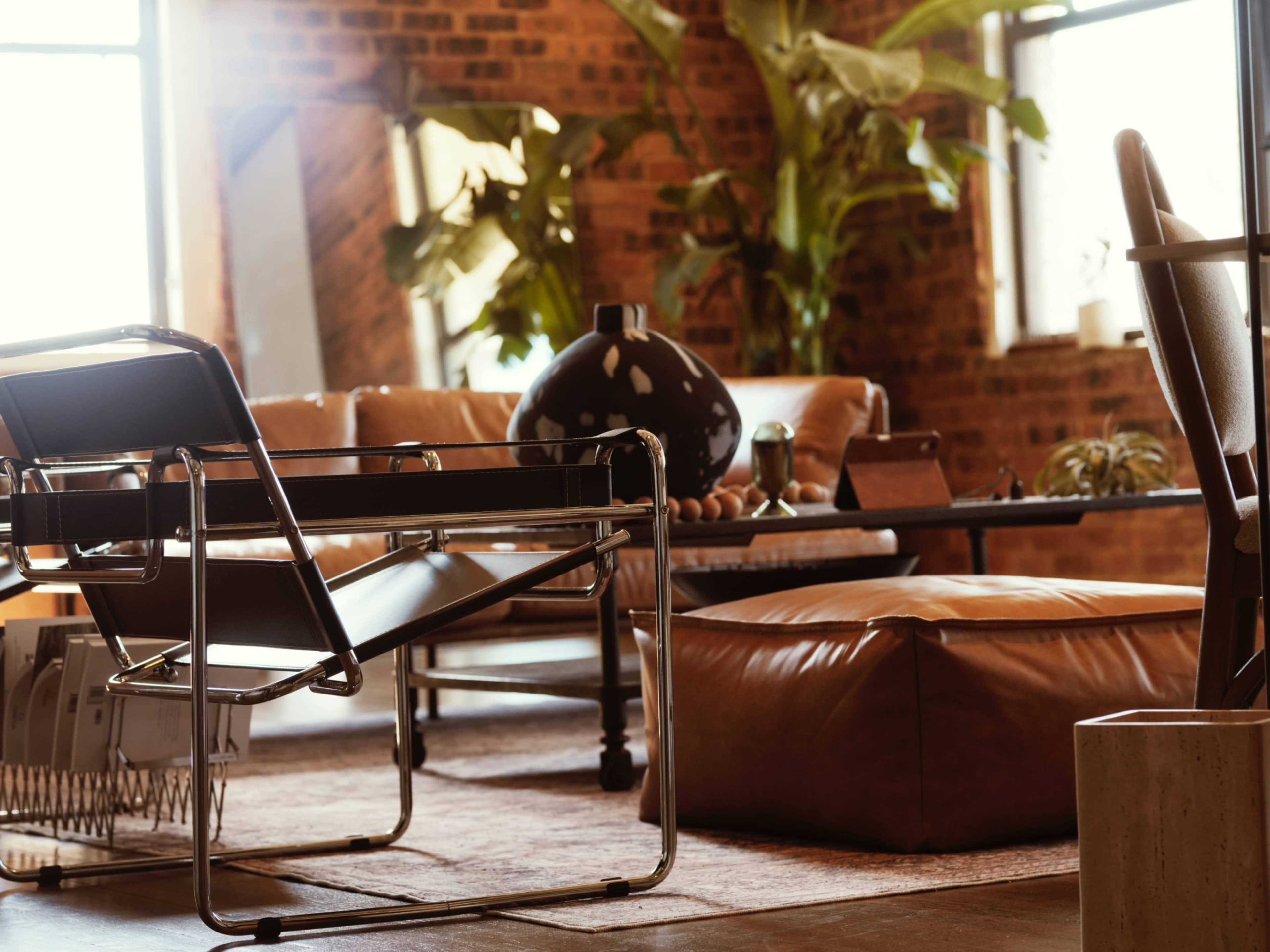 The image shows a cozy living room with a leather sofa, a large decorative vase, and plants, all set against a brick wall.