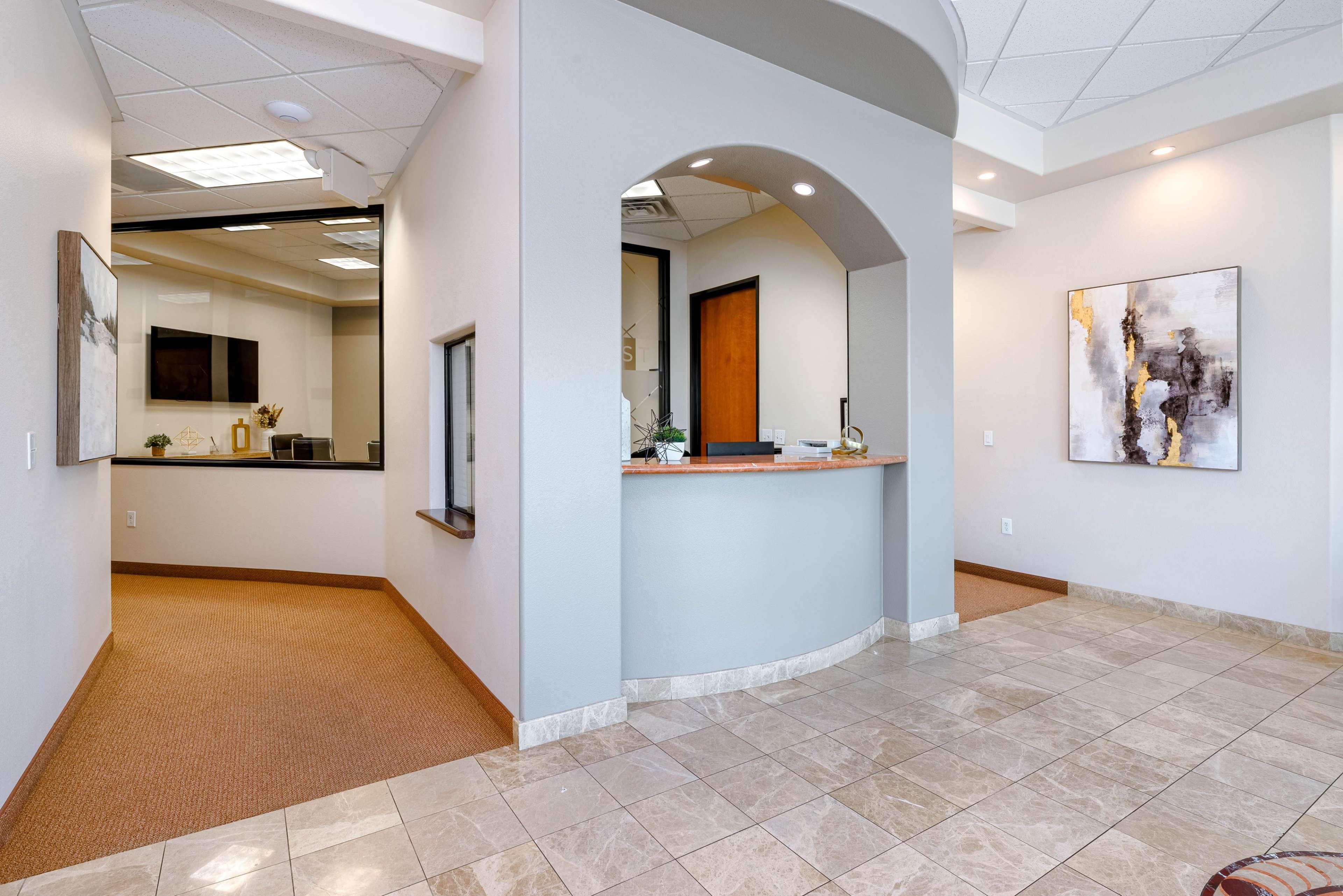 A modern reception area with a curved front desk, tiled flooring, and a doorway leading to another room.