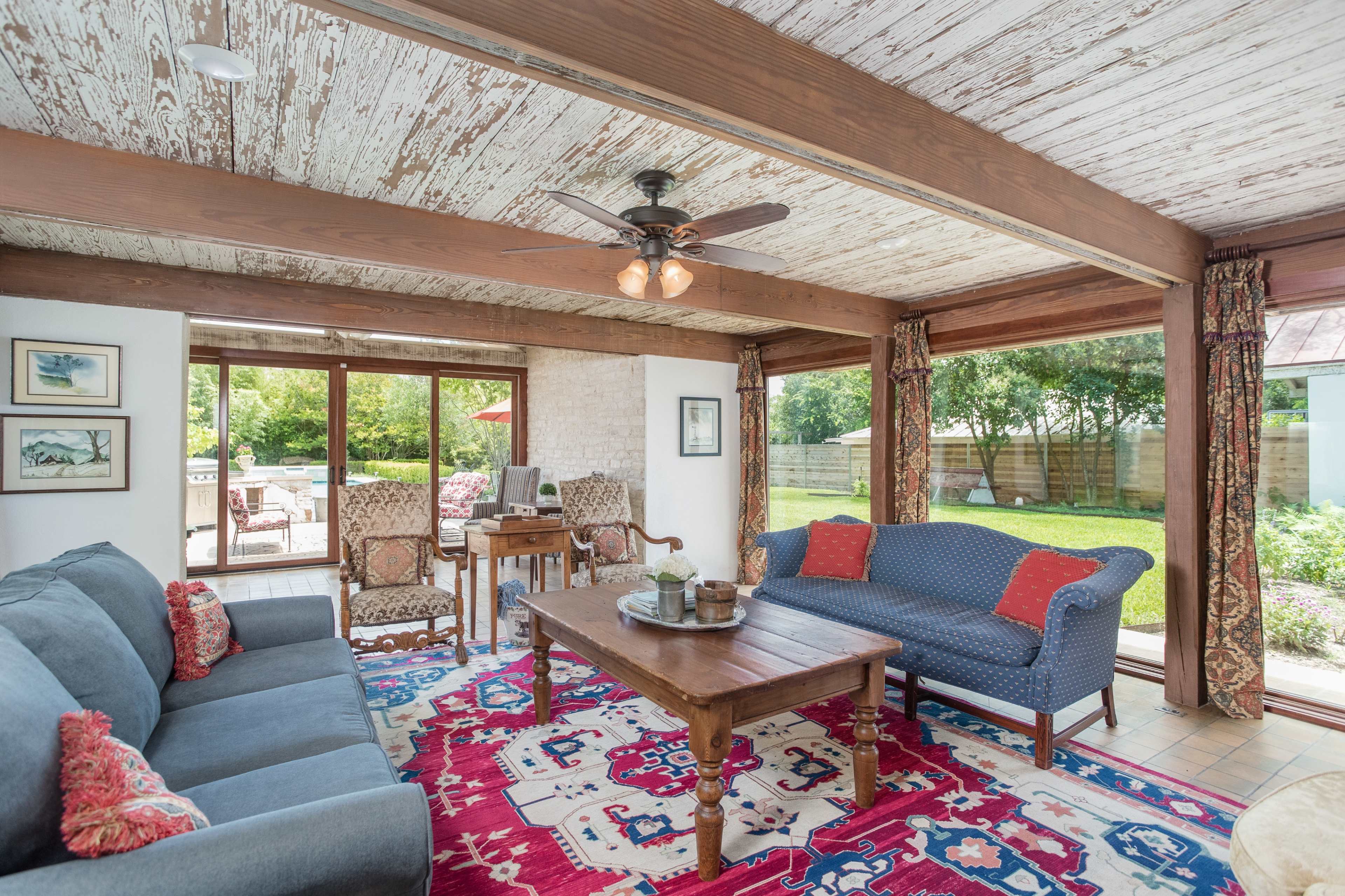 A bright living room features a blue couch, a wooden coffee table, and large windows overlooking a garden.