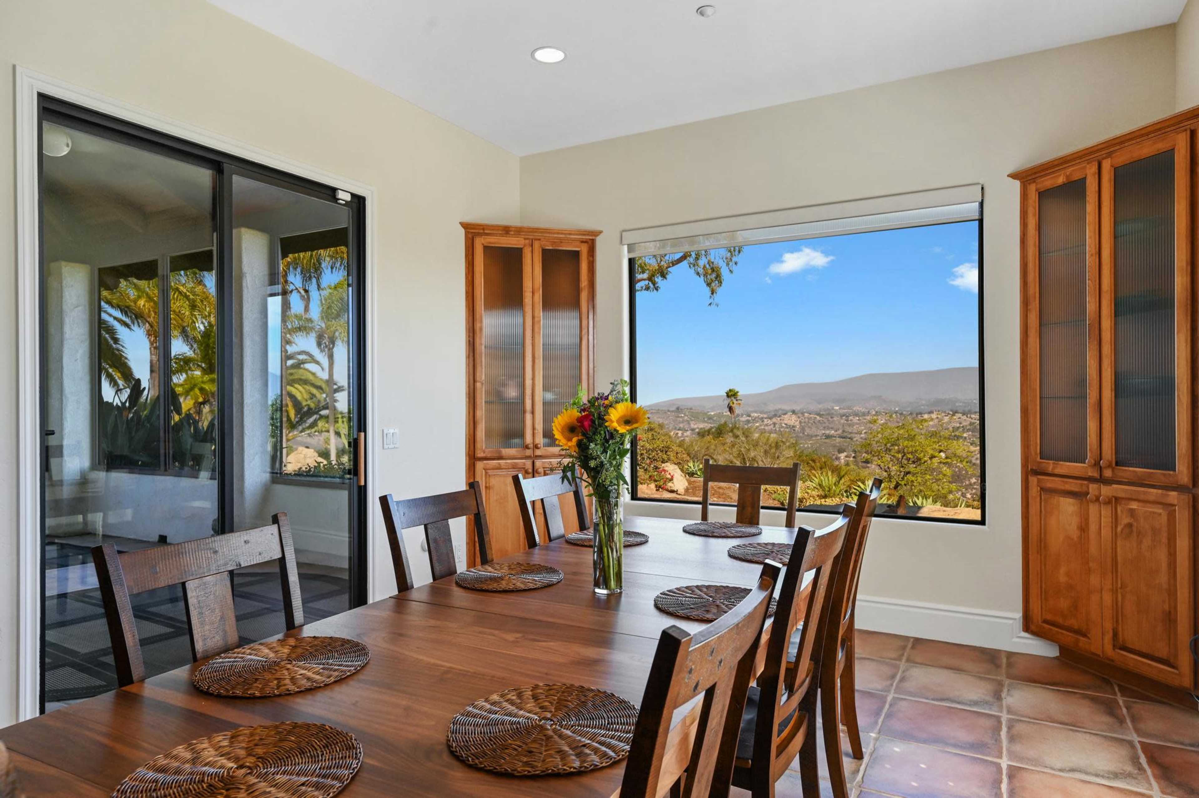 A spacious dining area features a wooden table surrounded by chairs and a large window showcasing a scenic view of the landscape.
