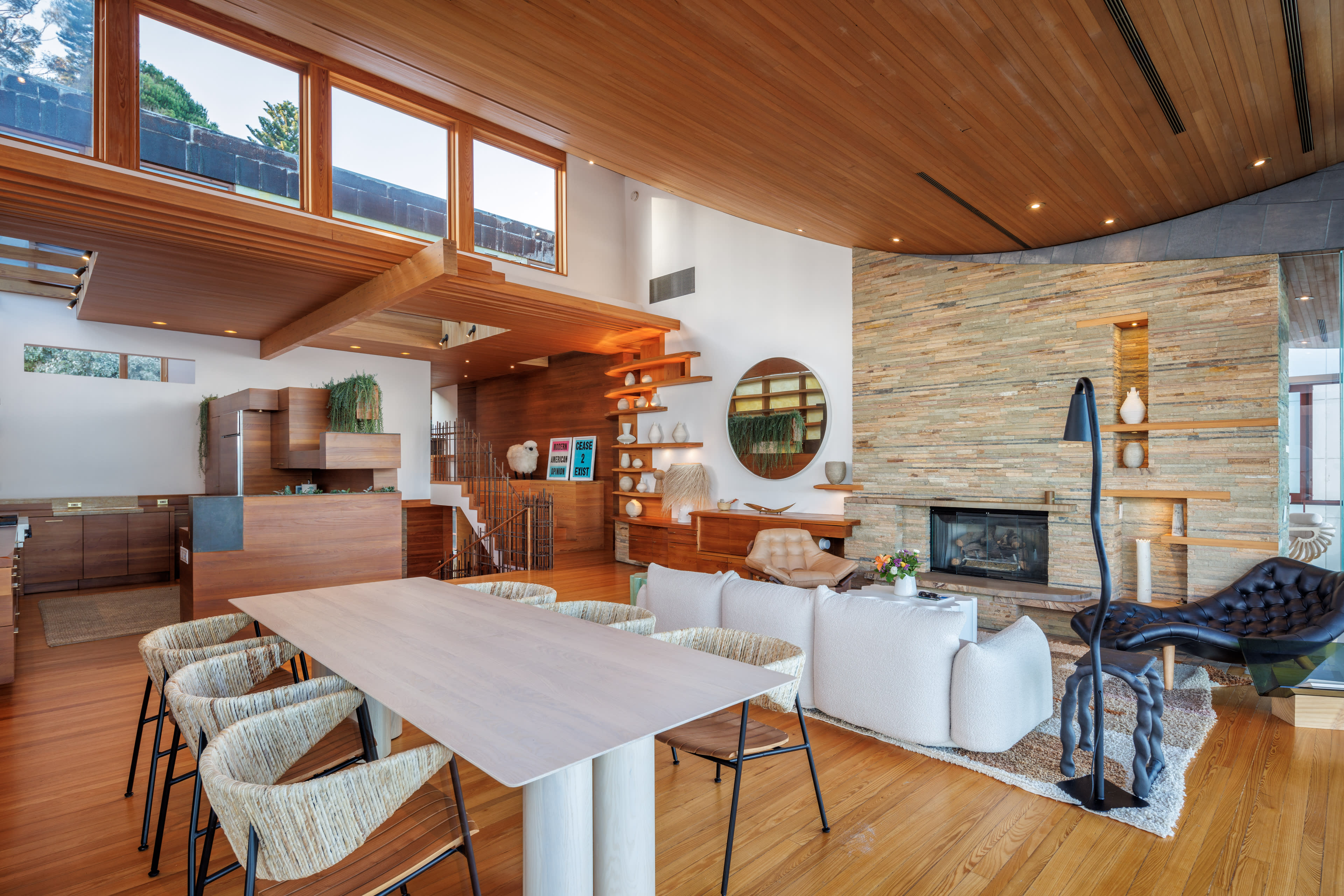 A modern living area with wooden ceilings, a stone fireplace, and a dining table surrounded by upholstered chairs.