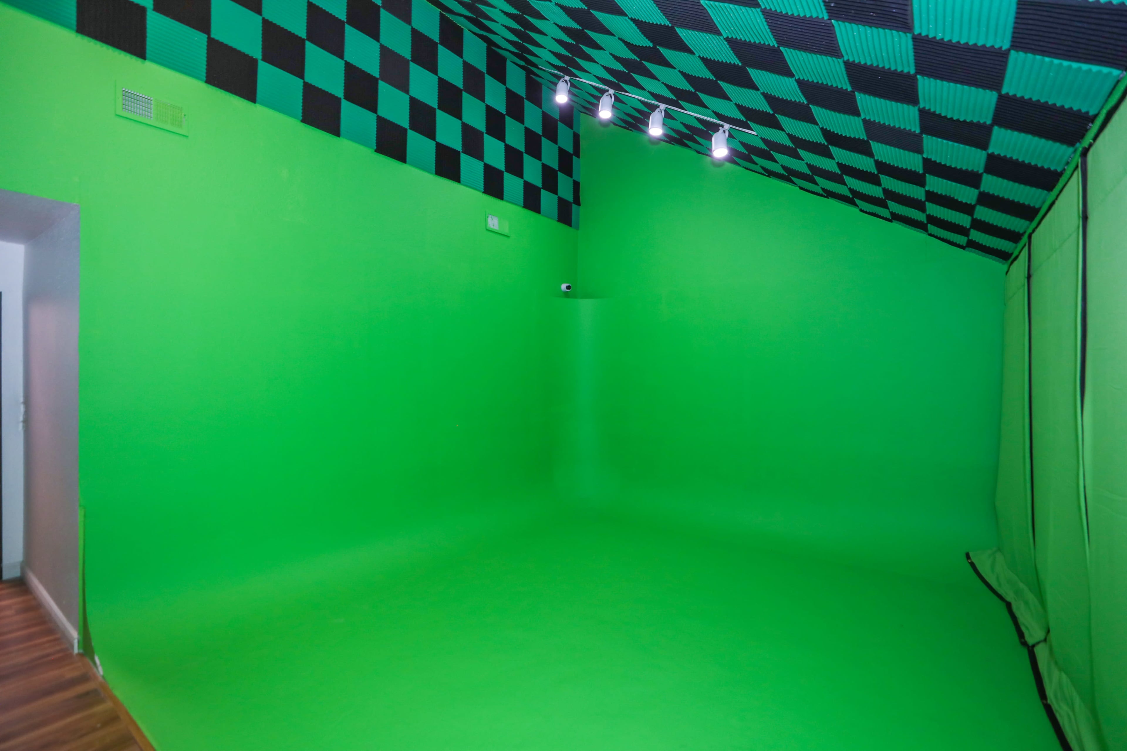 The image shows a green room designed for video production, featuring green walls and flooring with a black and green checkered ceiling.