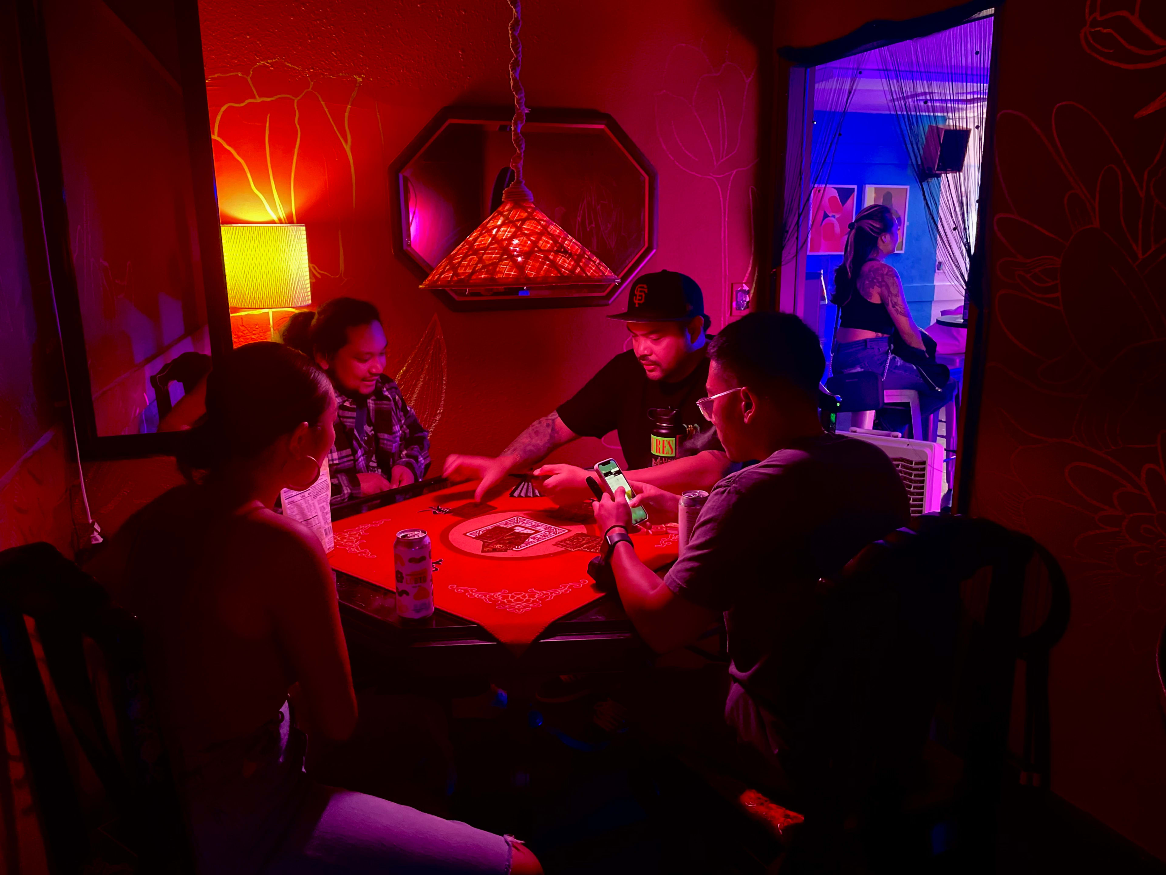 A group of four people gathers around a table in a dimly lit room adorned with colorful lighting.