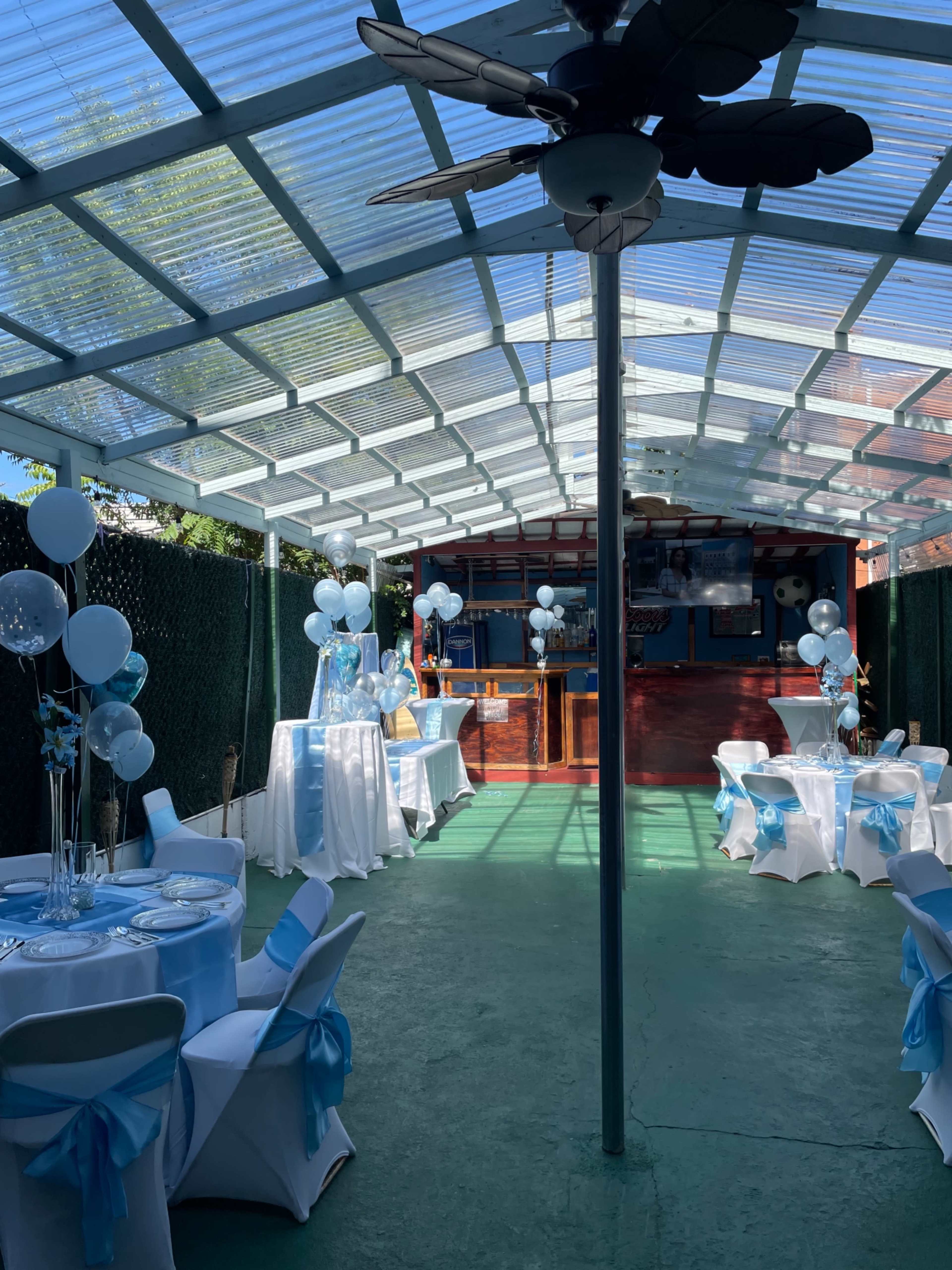 An outdoor party space with decorated tables and balloons arranged in a canopy-covered area.