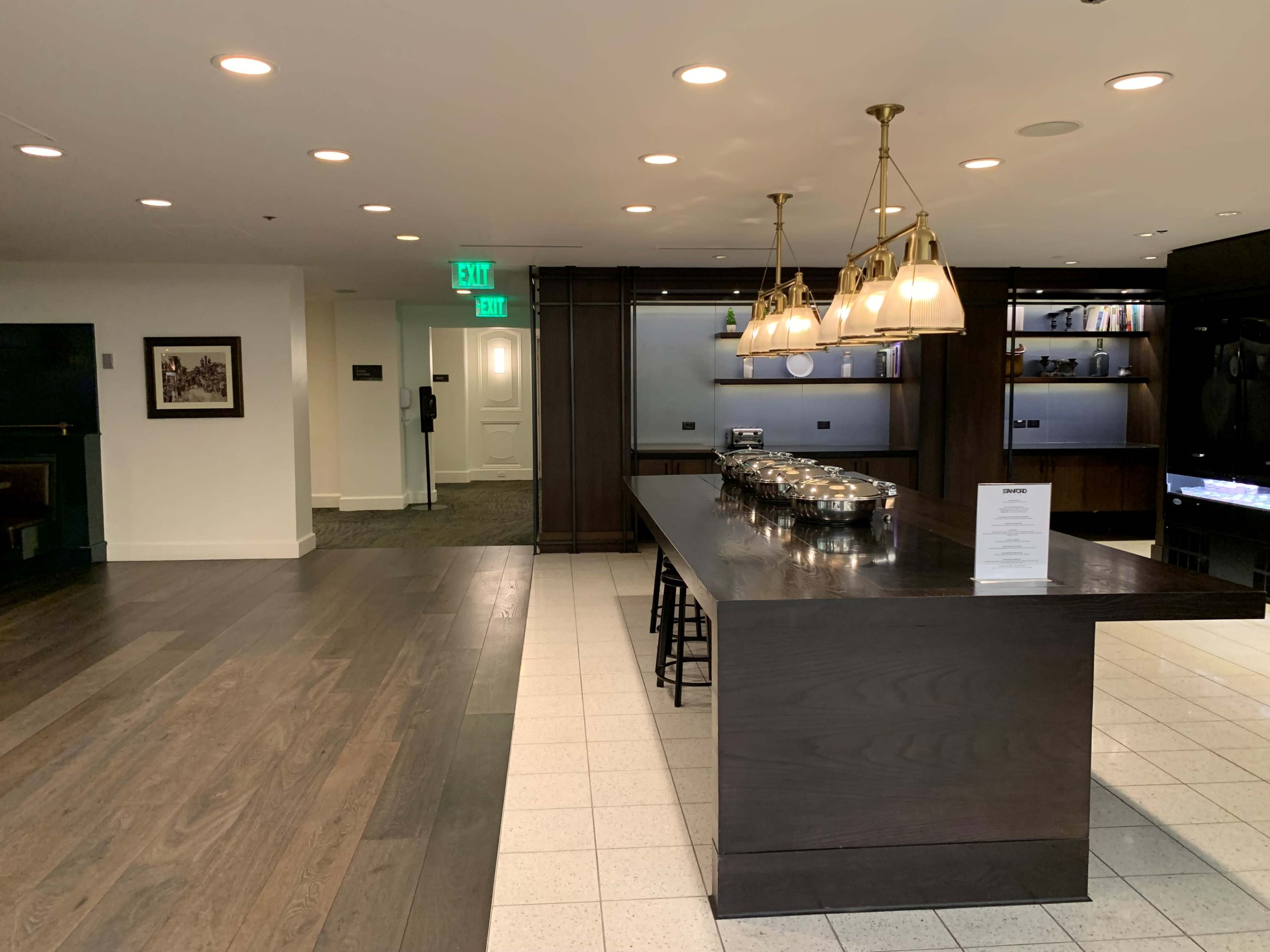 The image shows a modern interior space featuring a dark wooden island with containers, overhead lighting, and a doorway leading to another room.