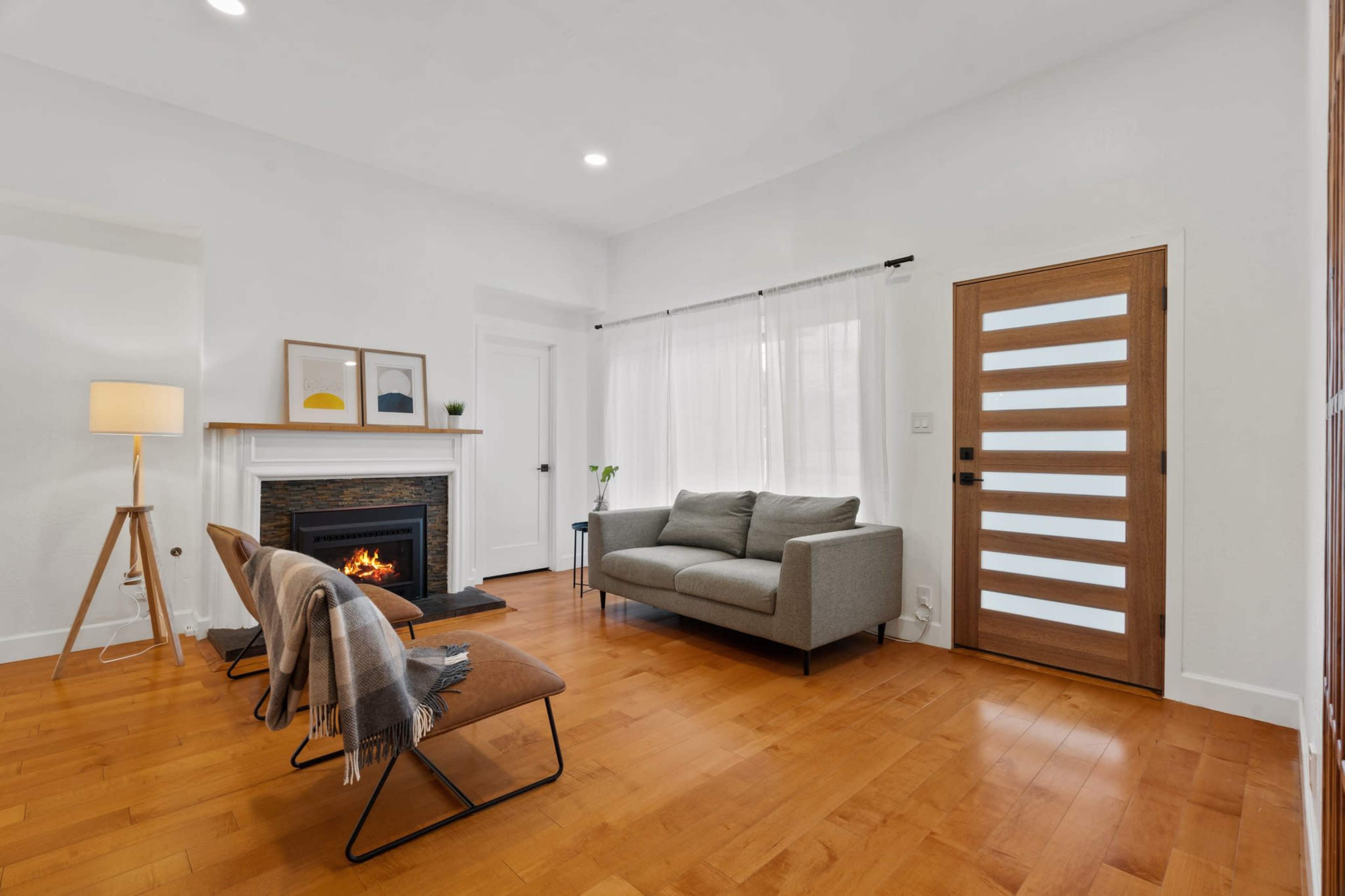 A modern living room featuring a gray sofa, two wooden chairs with blankets, a fireplace, and a door with horizontal slats.