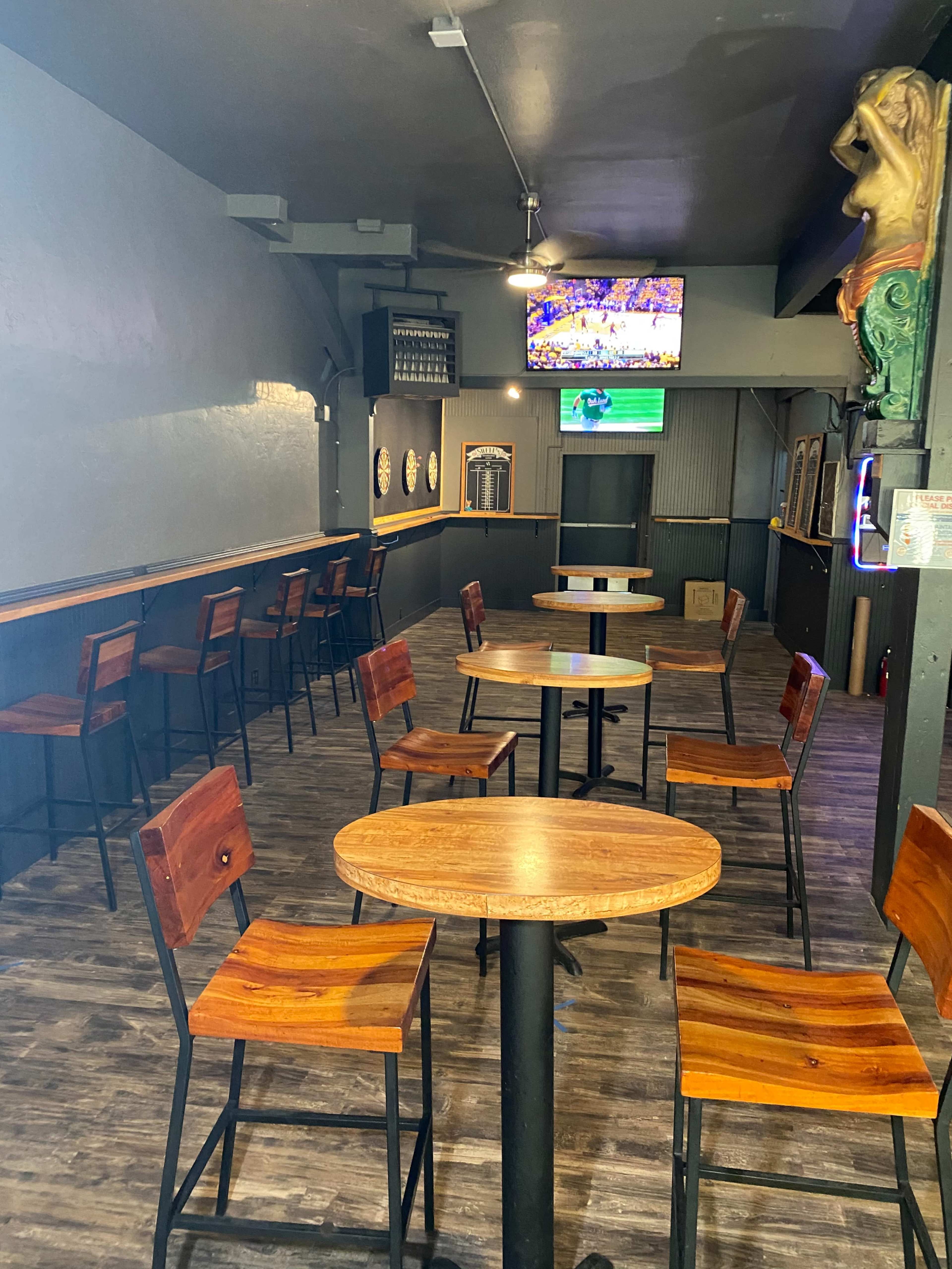 The image shows a bar area with wooden tables and chairs, a television displaying a sports game, and a dimly lit interior.