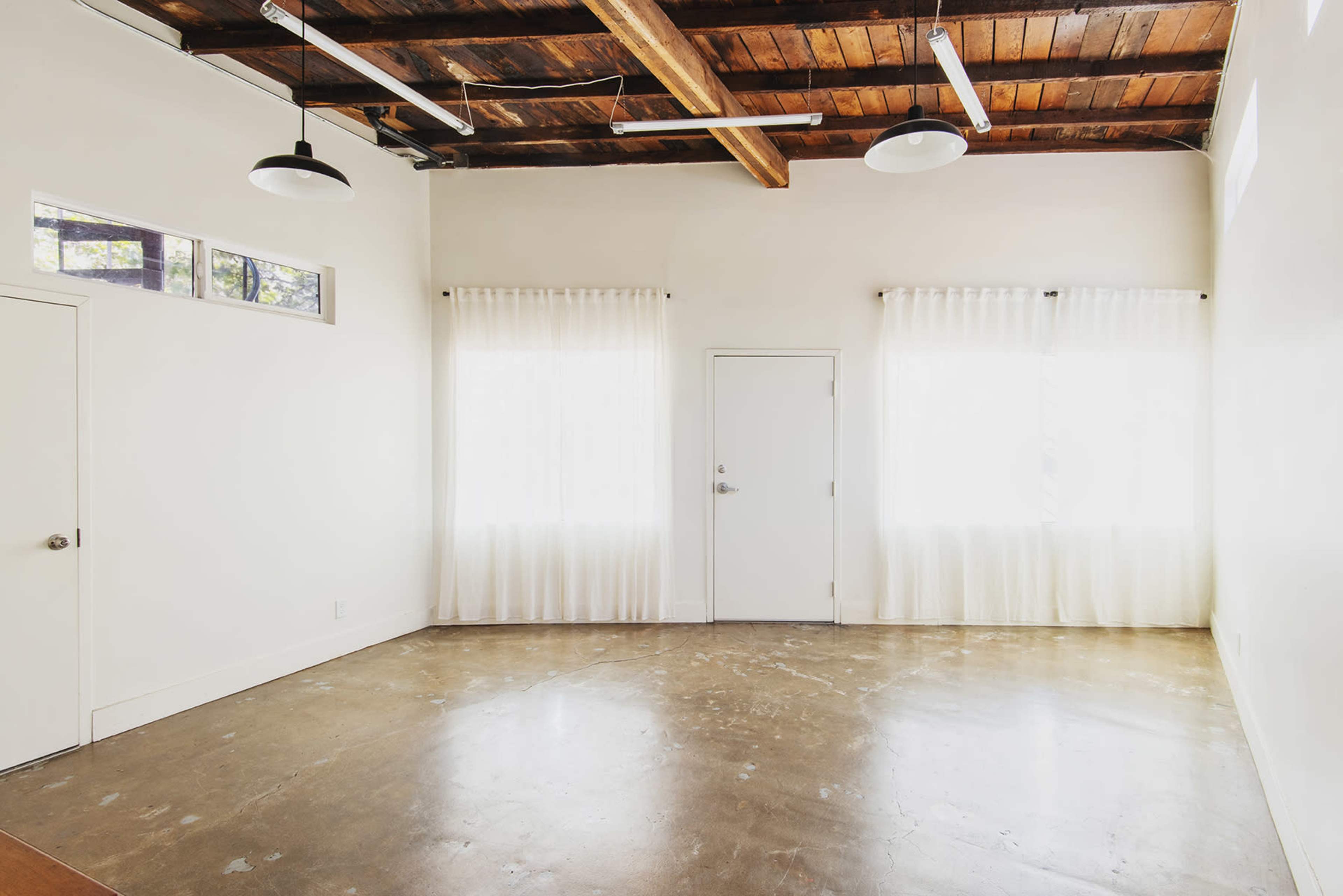 The image shows an empty room with a polished concrete floor, white walls, and large windows with sheer curtains.