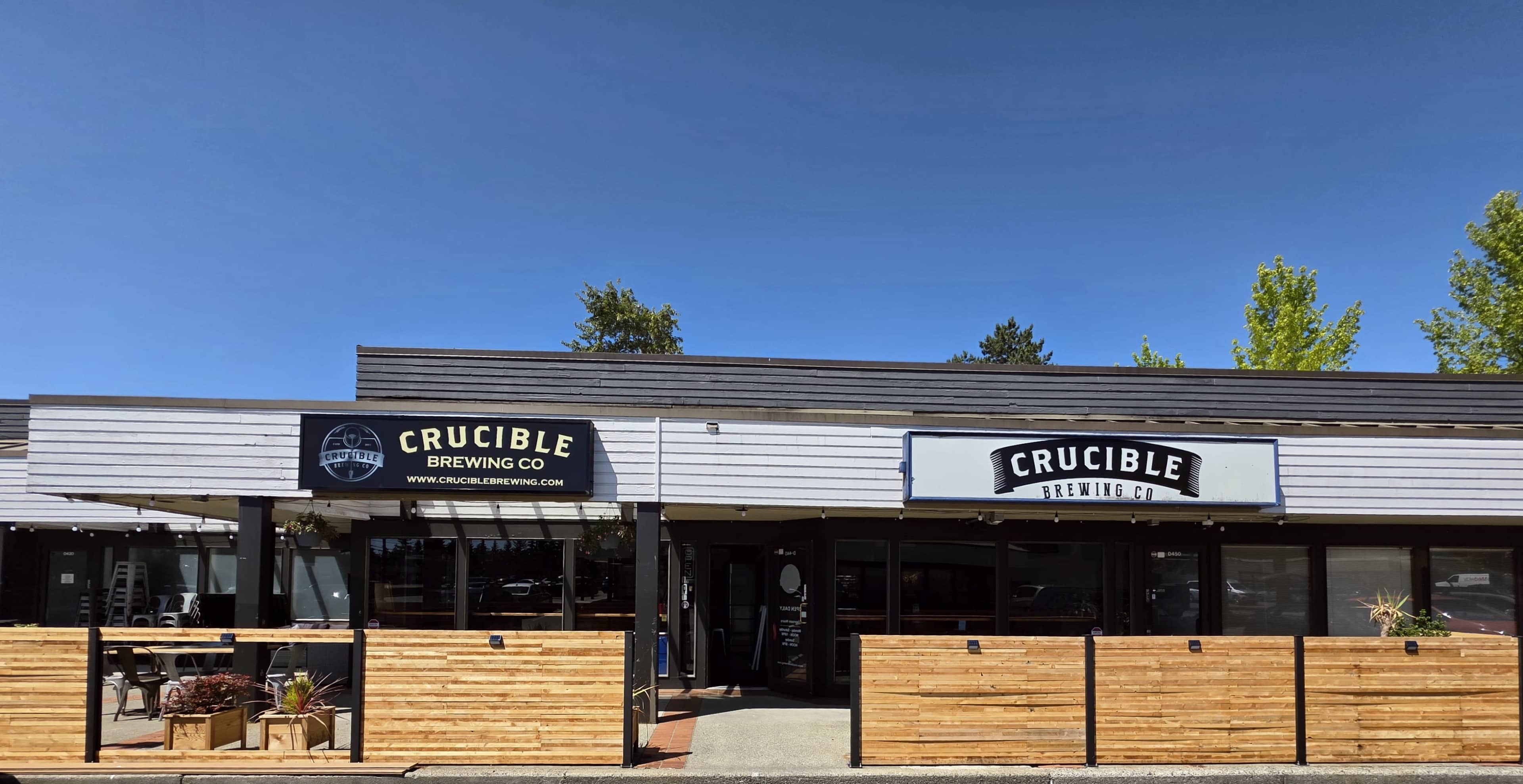 The image shows the exterior of Crucible Brewing Co, featuring a wooden fence in front, with signage indicating the brewery's name and website.