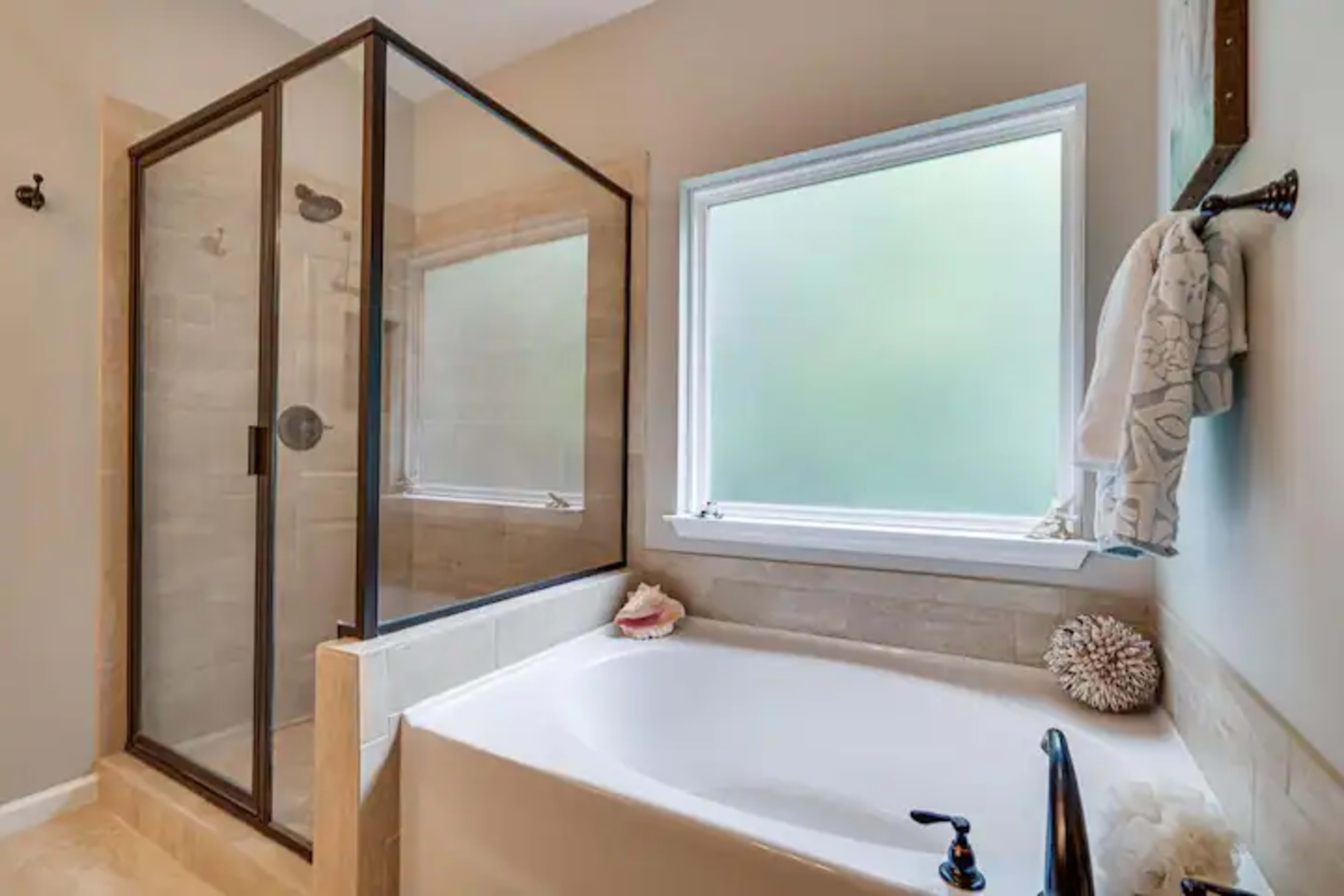 A modern bathroom featuring a glass-enclosed shower, a white bathtub, and a window providing natural light.