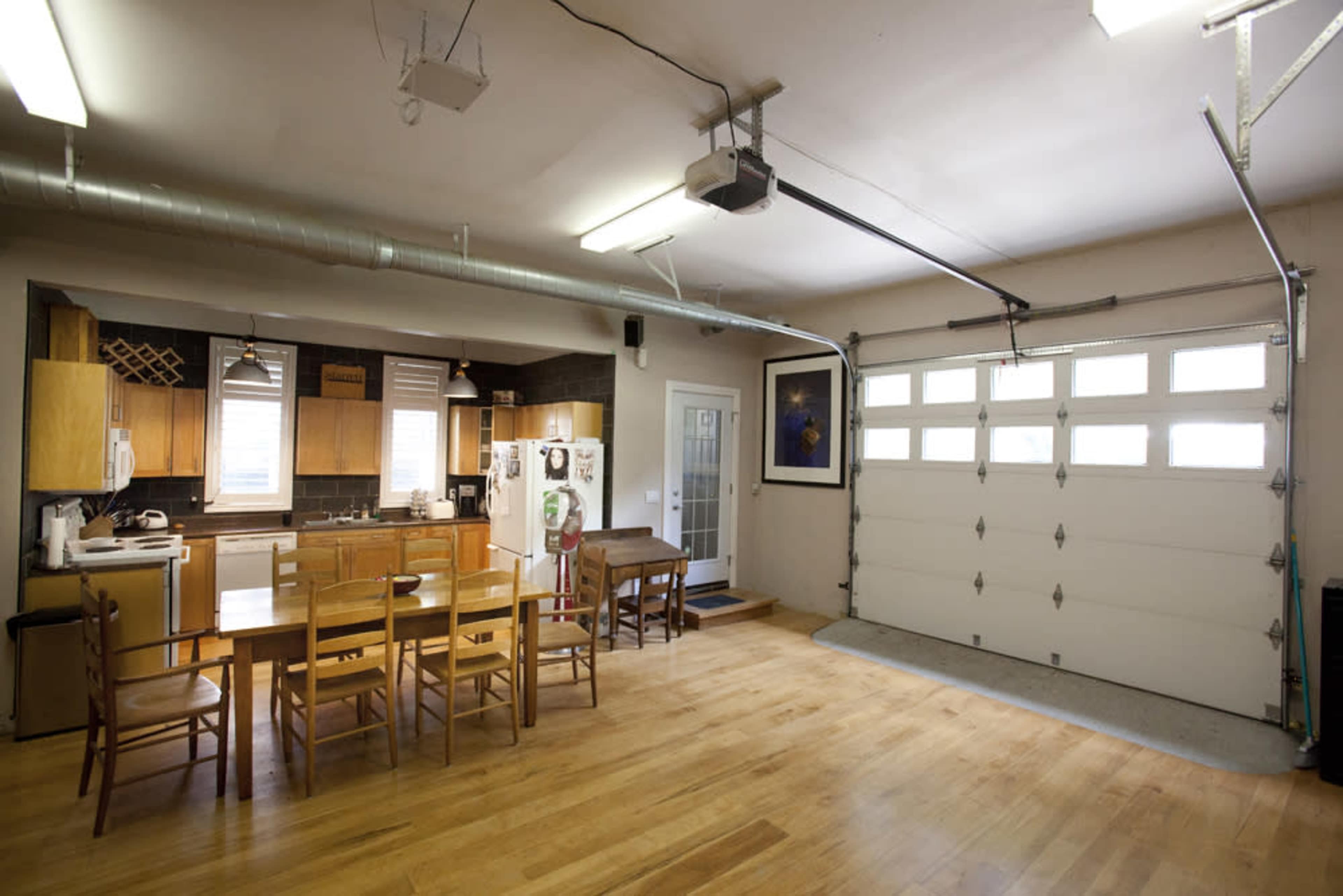 A spacious garage converted into a kitchen and dining area with wooden floors, a dining table, and a roll-up door.