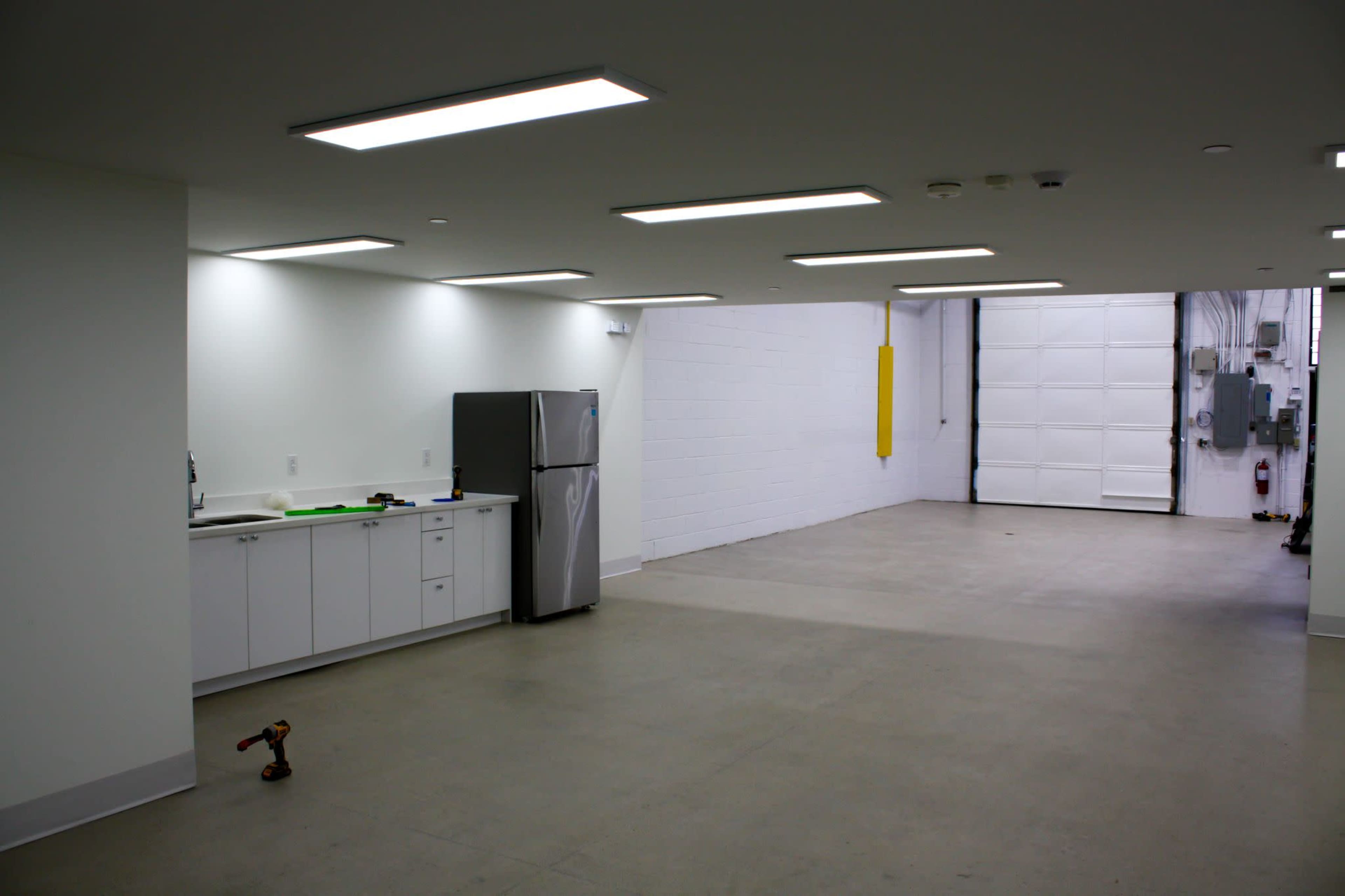 A spacious, empty garage with a kitchenette area on one side and a large roll-up door at the far end.