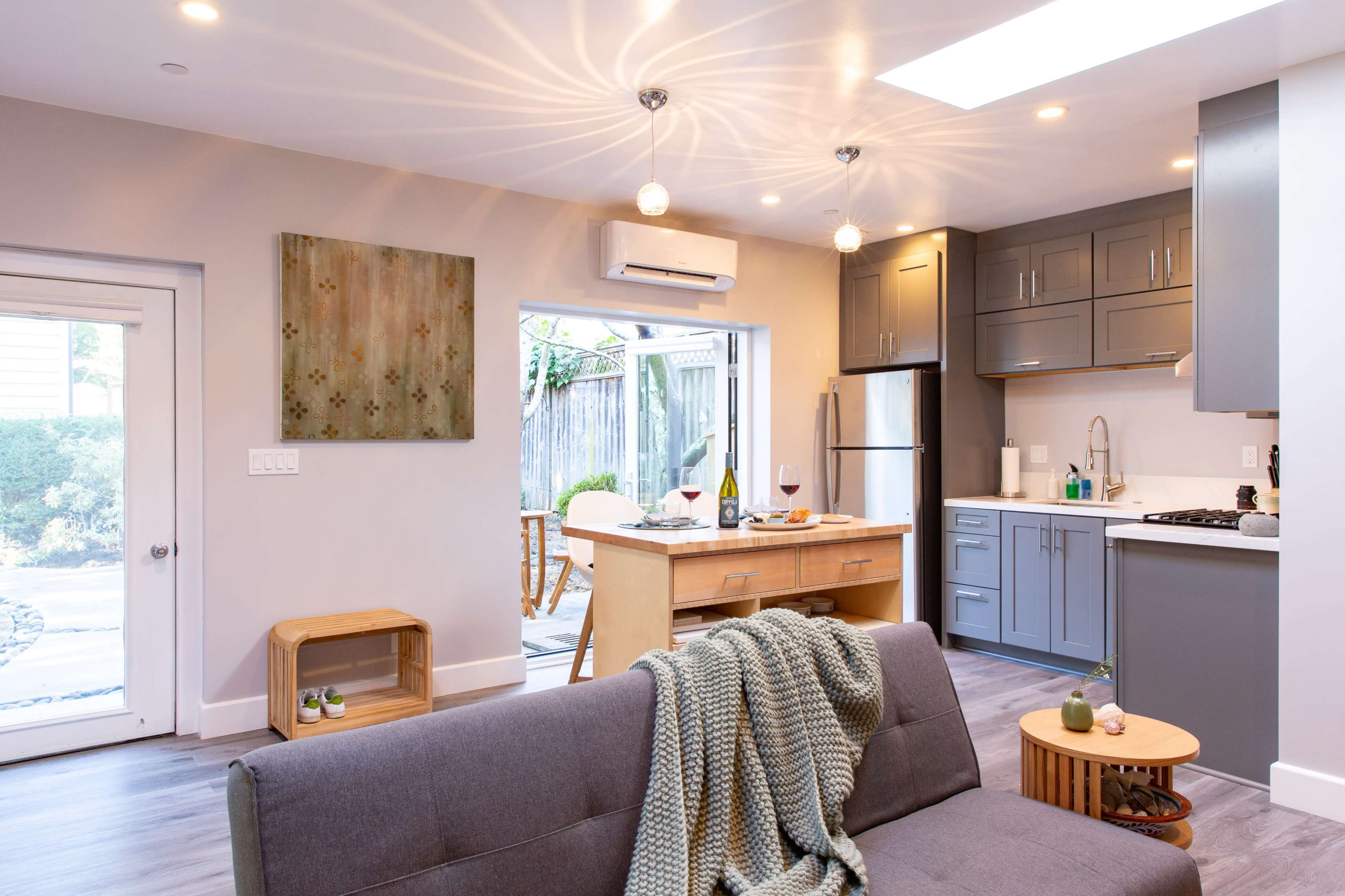 A modern kitchen and living area feature sleek cabinetry, open access to an outdoor space, and cozy furnishings.