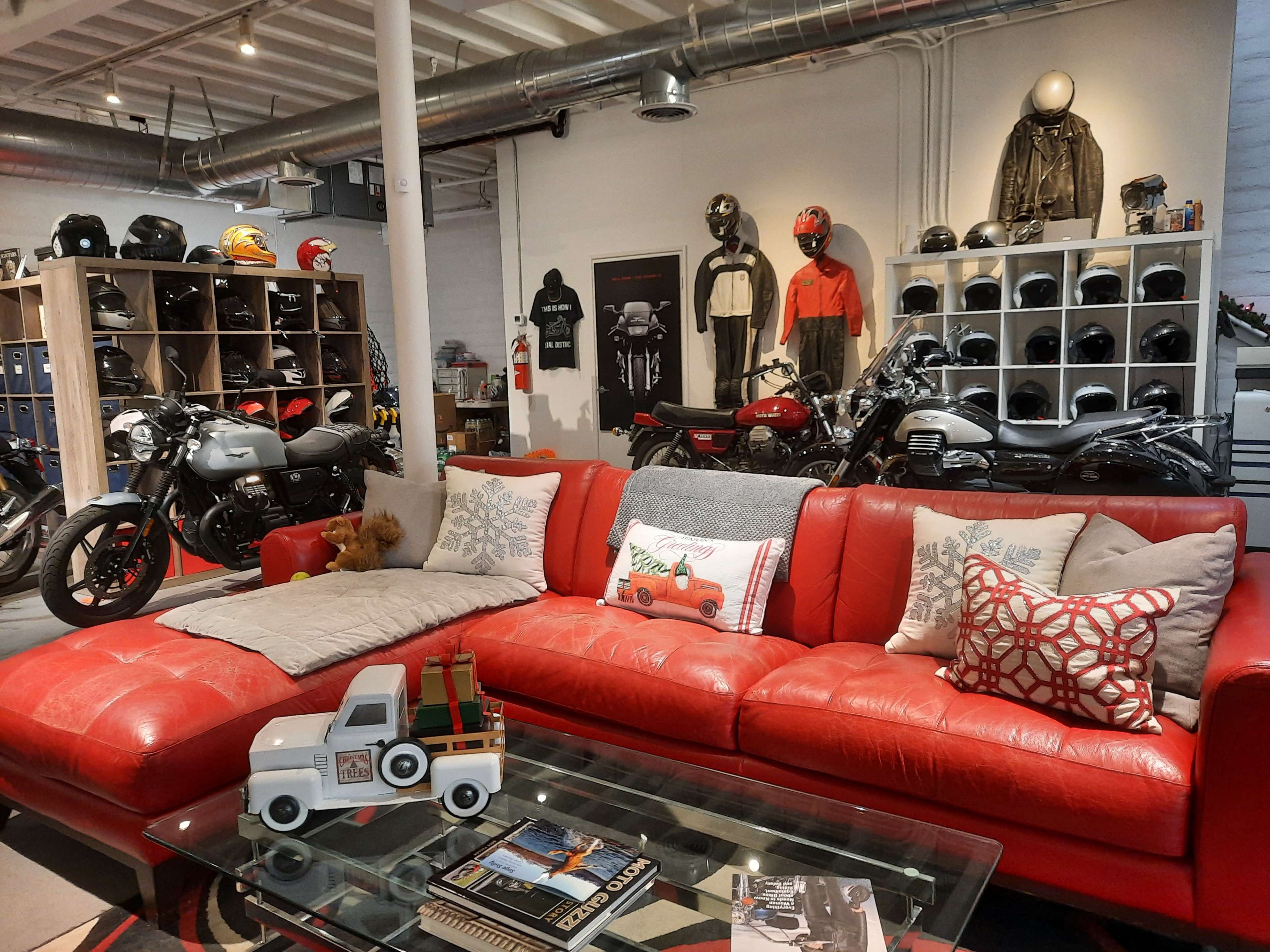 A spacious room featuring a red leather sofa, a glass coffee table with books, and a collection of motorcycles and helmets displayed on shelves.
