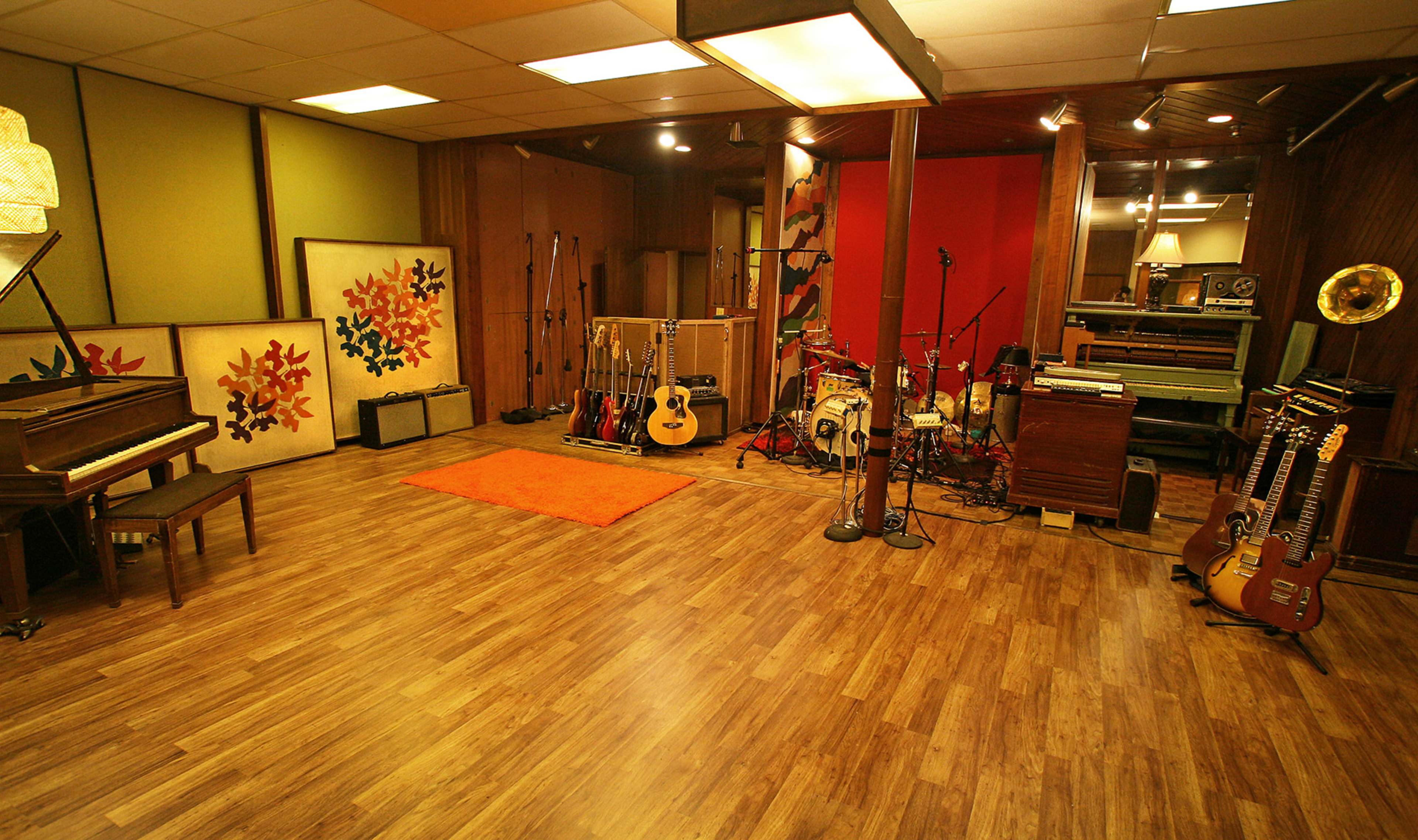 A spacious recording studio with a piano, various musical instruments, colorful wall art, and sound equipment.