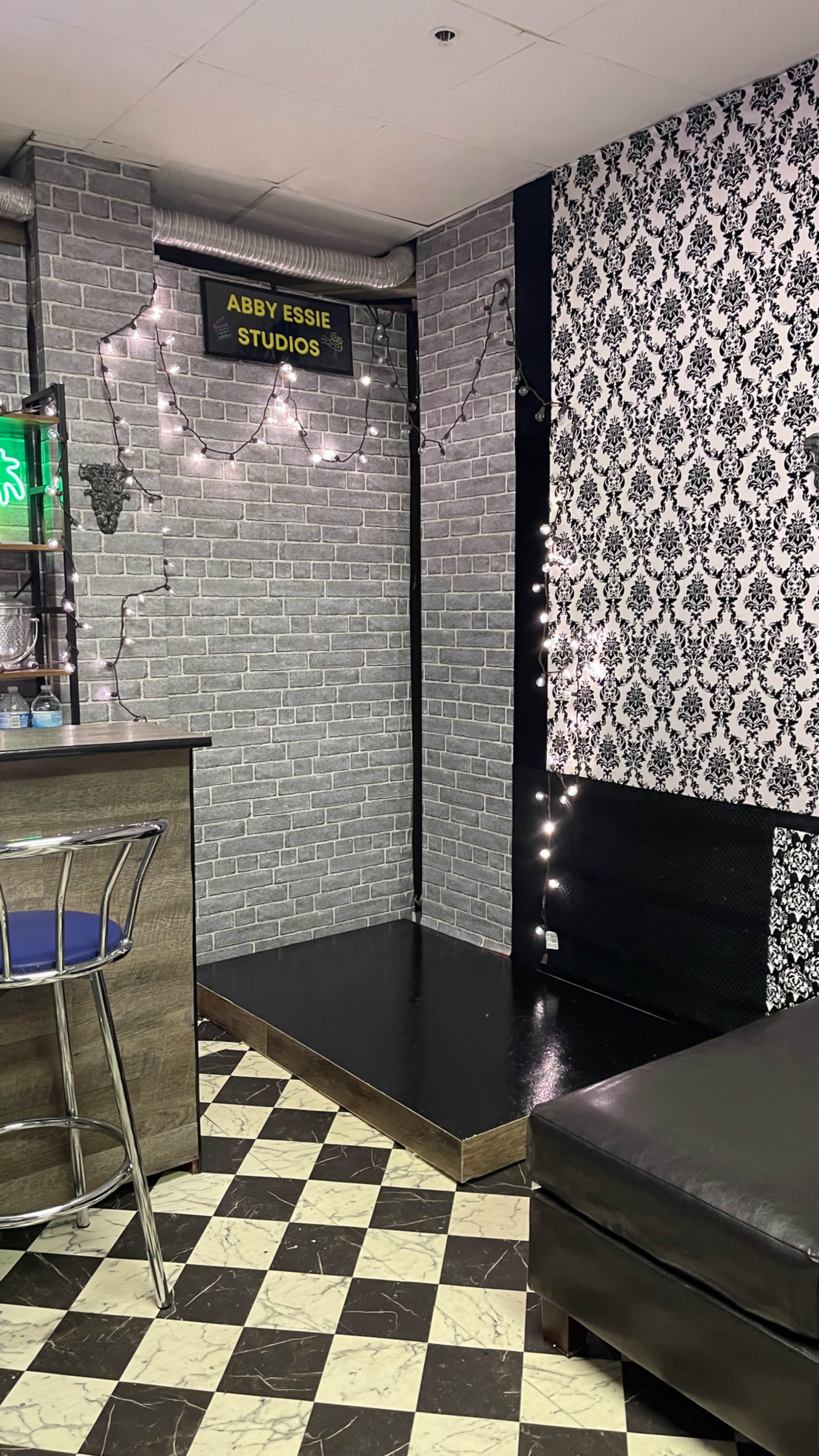 The image shows a small studio space with patterned walls, a black and white checkered floor, and a bar counter in one corner.