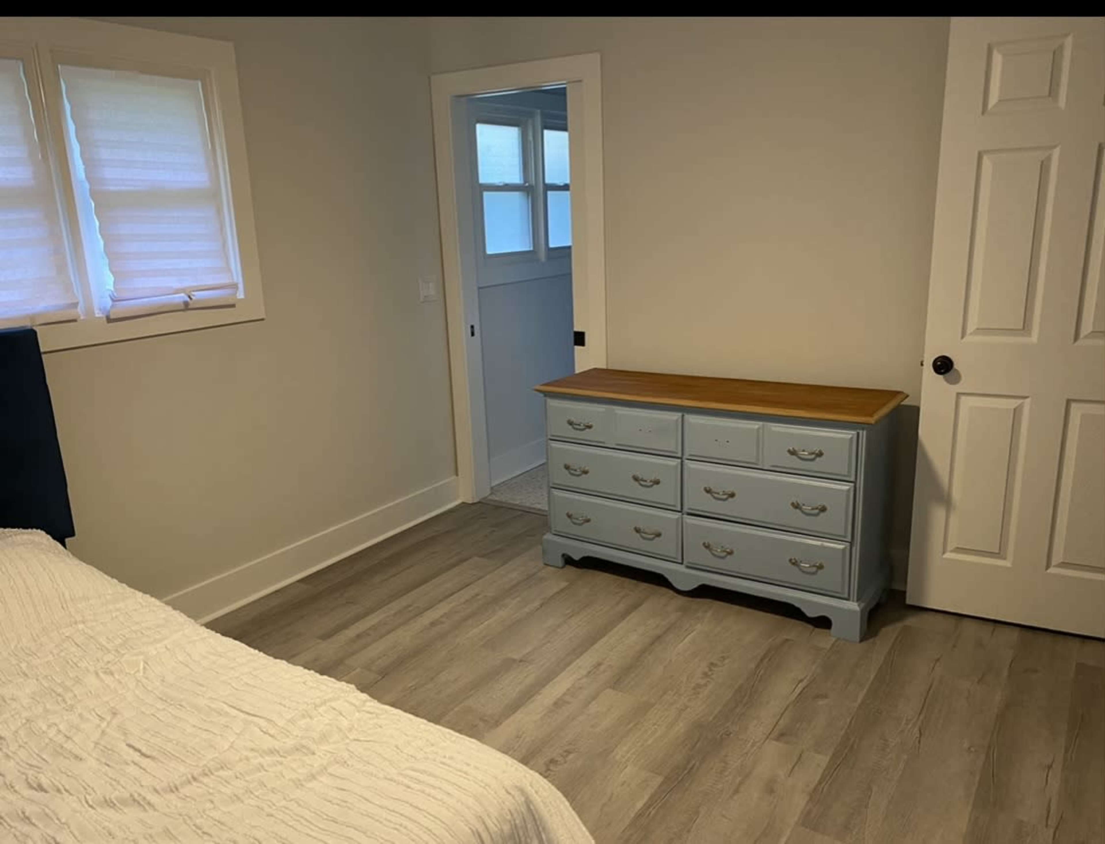 A light-colored room with a blue dresser against the wall and a door leading to another room.